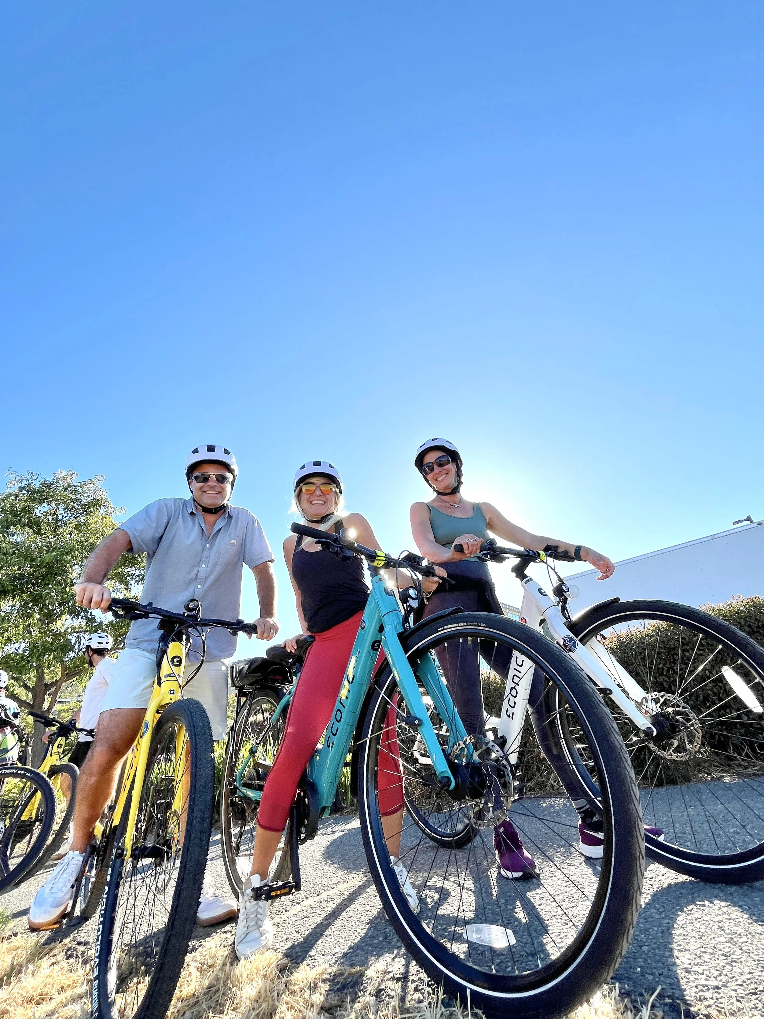 Three people wearing helmets with bikes, standing outdoors under a blue sky during daytime.