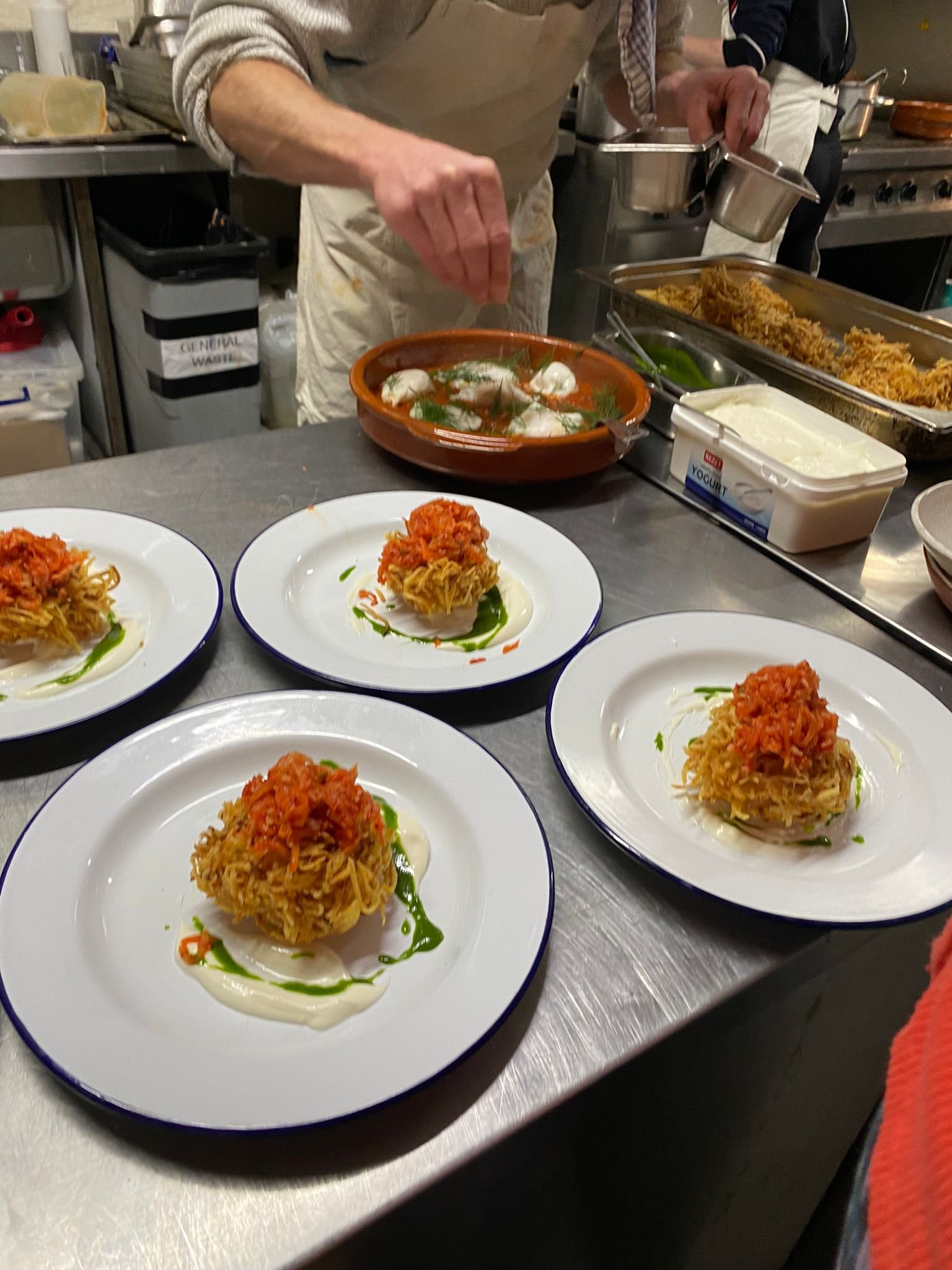 Chef plating fried crab cakes topped with tomato salsa on white plates in a busy kitchen.