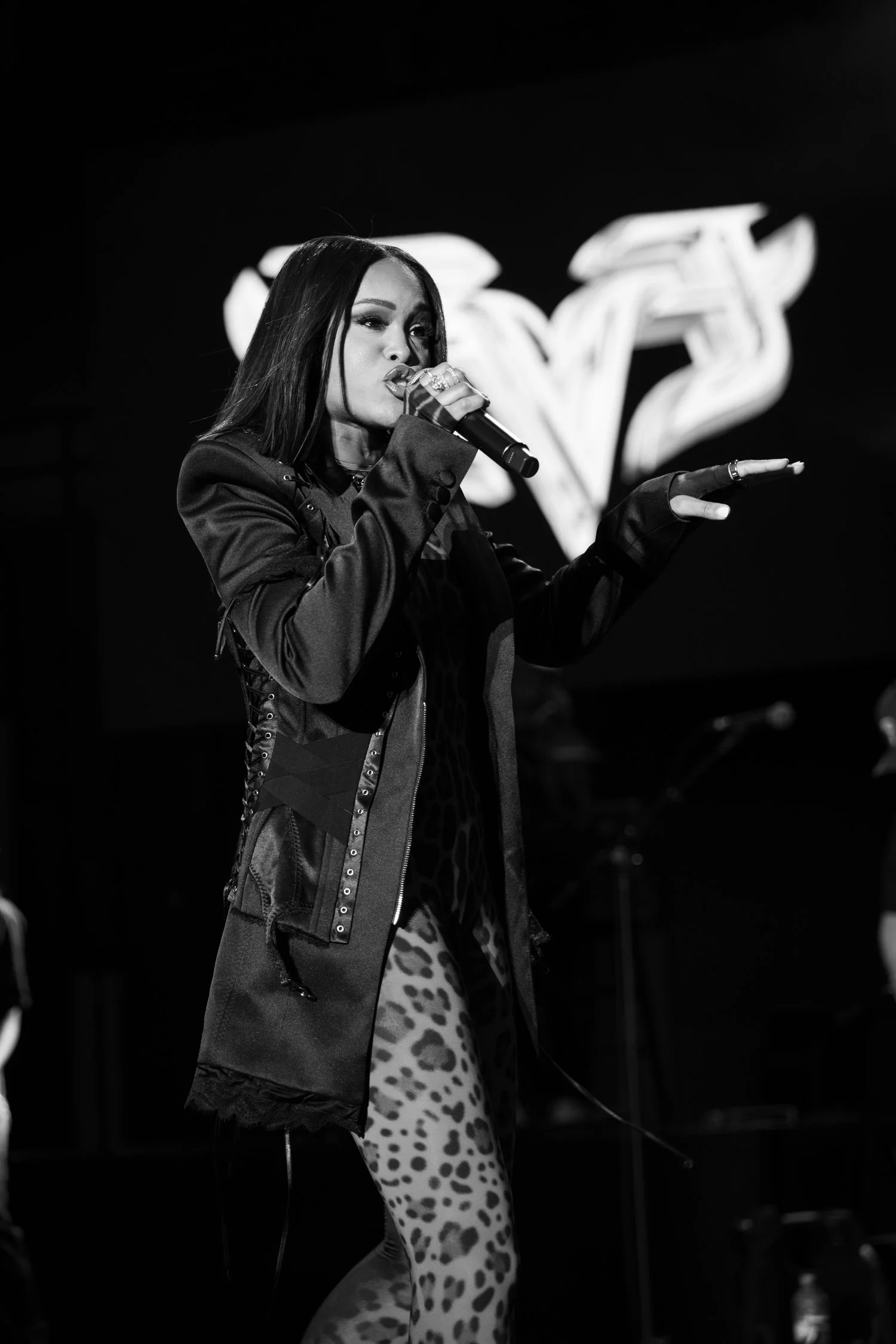 Black-and-white concert photograph of Eve singing into a microphone with one hand extended.