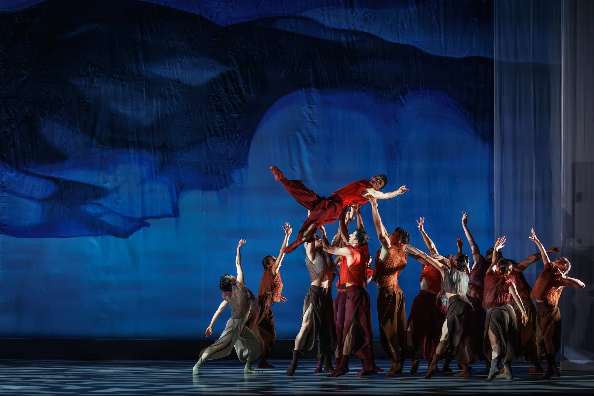 BalletX dancers performing an ensemble lift on a blue-lit stage