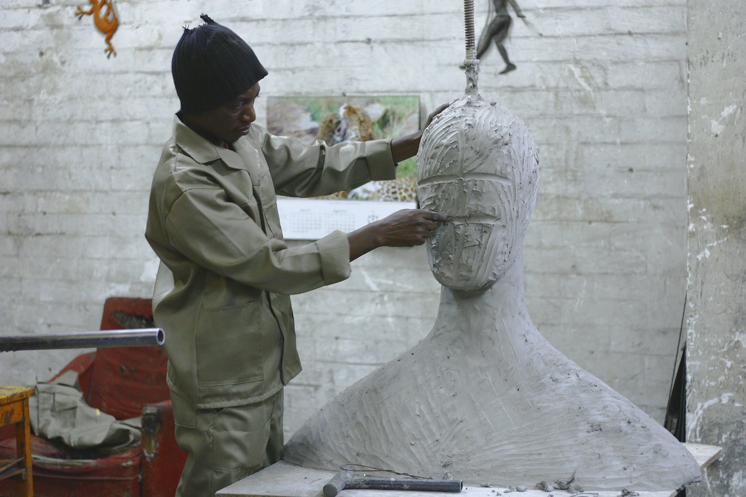 A man is carving a large clay head which shows the material has the potential to become something of the man's choosing, or not.