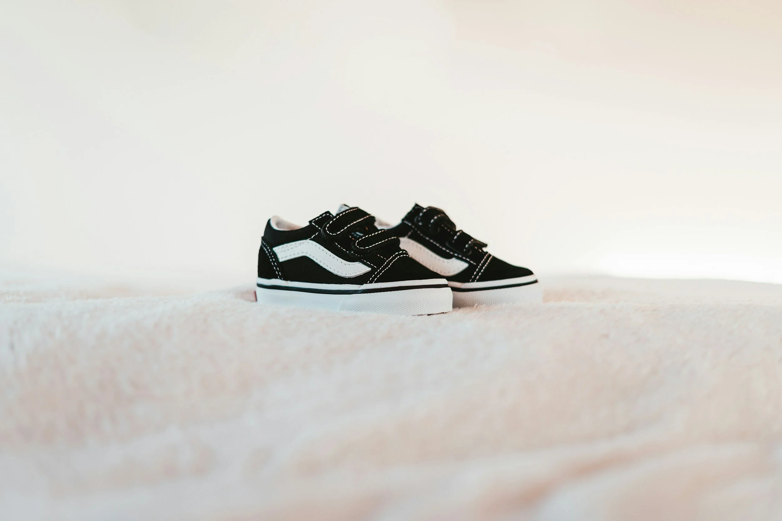 A pair of black and white baby shoes sit on a white blanket. We all start with  a first faith.