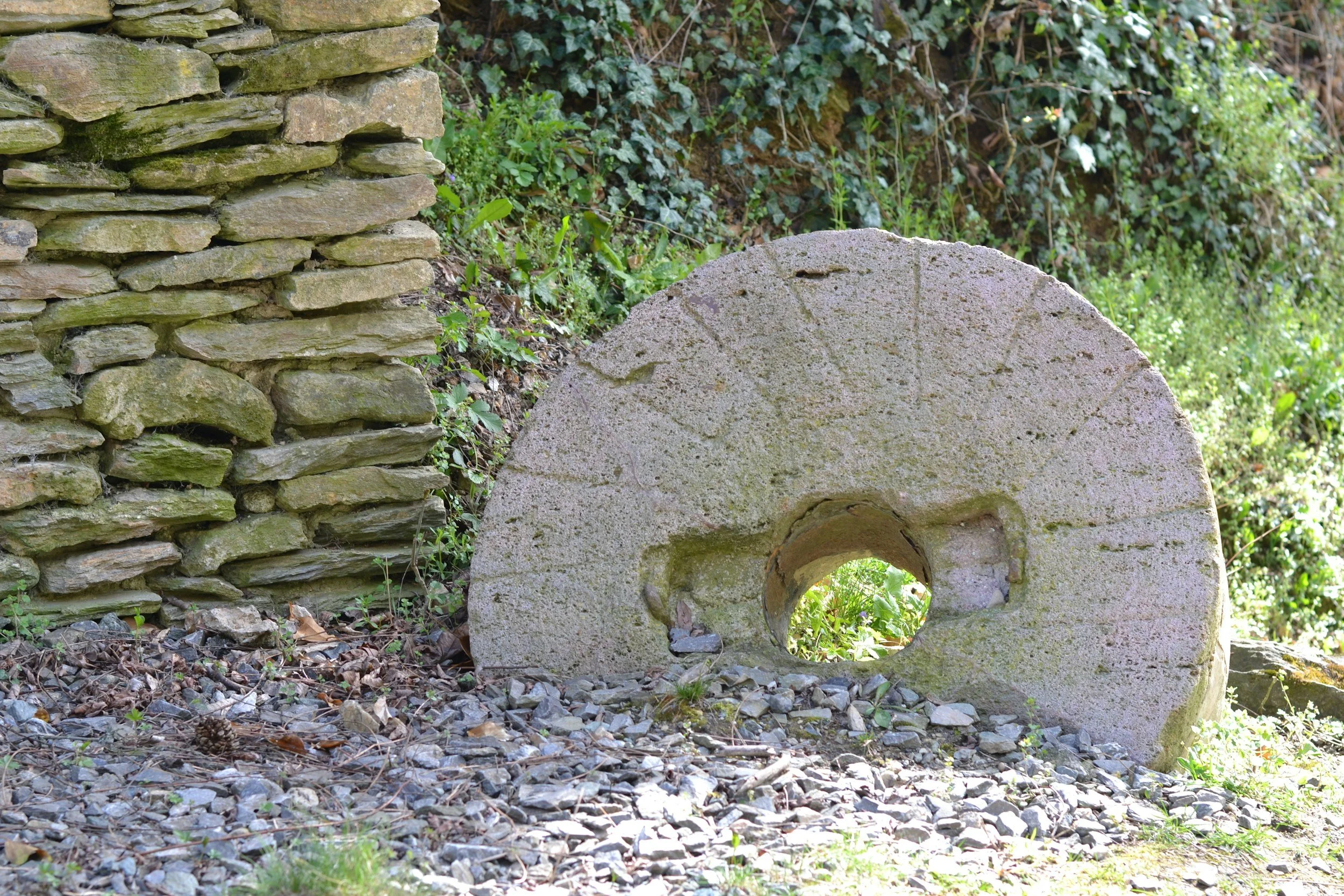 A large millstone rests against a sturdy stone wall.