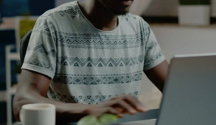 Person wearing a patterned t-shirt working on a laptop at a desk.