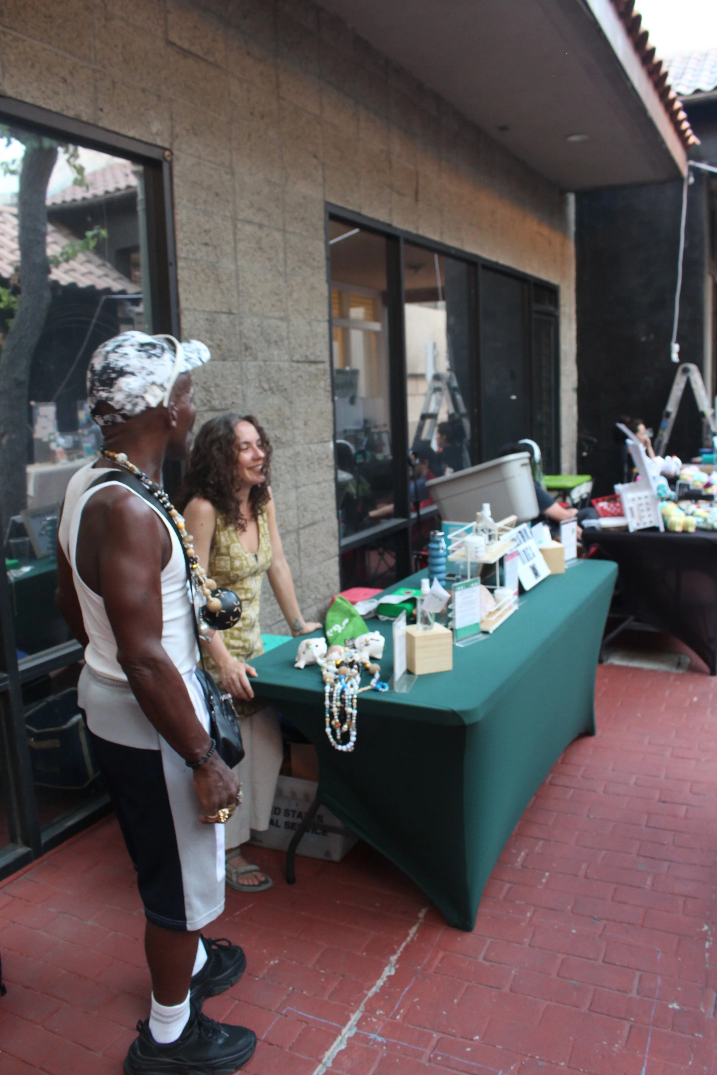 Two women are standing at a table displaying jewelry and small craft items at an outdoor market.
