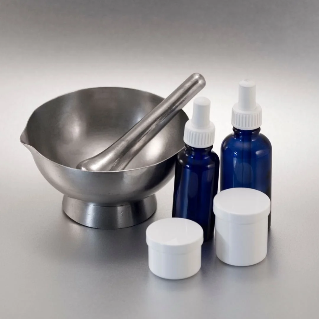 A metal bowl with a pestle, two small blue bottles with droppers, and two white jars on a grey surface.