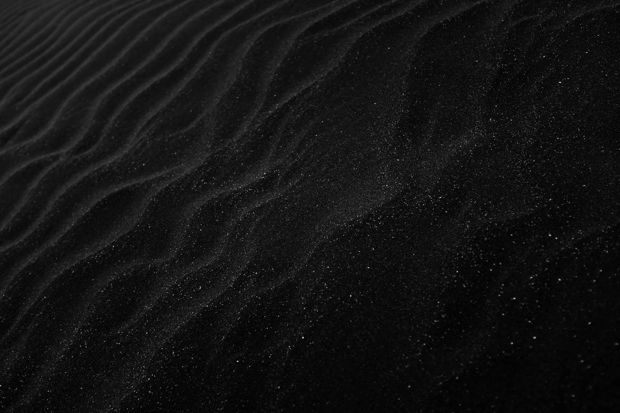 Close-up photo of a textured, black surface with fine, sparkling particles and subtle wave-like patterns.