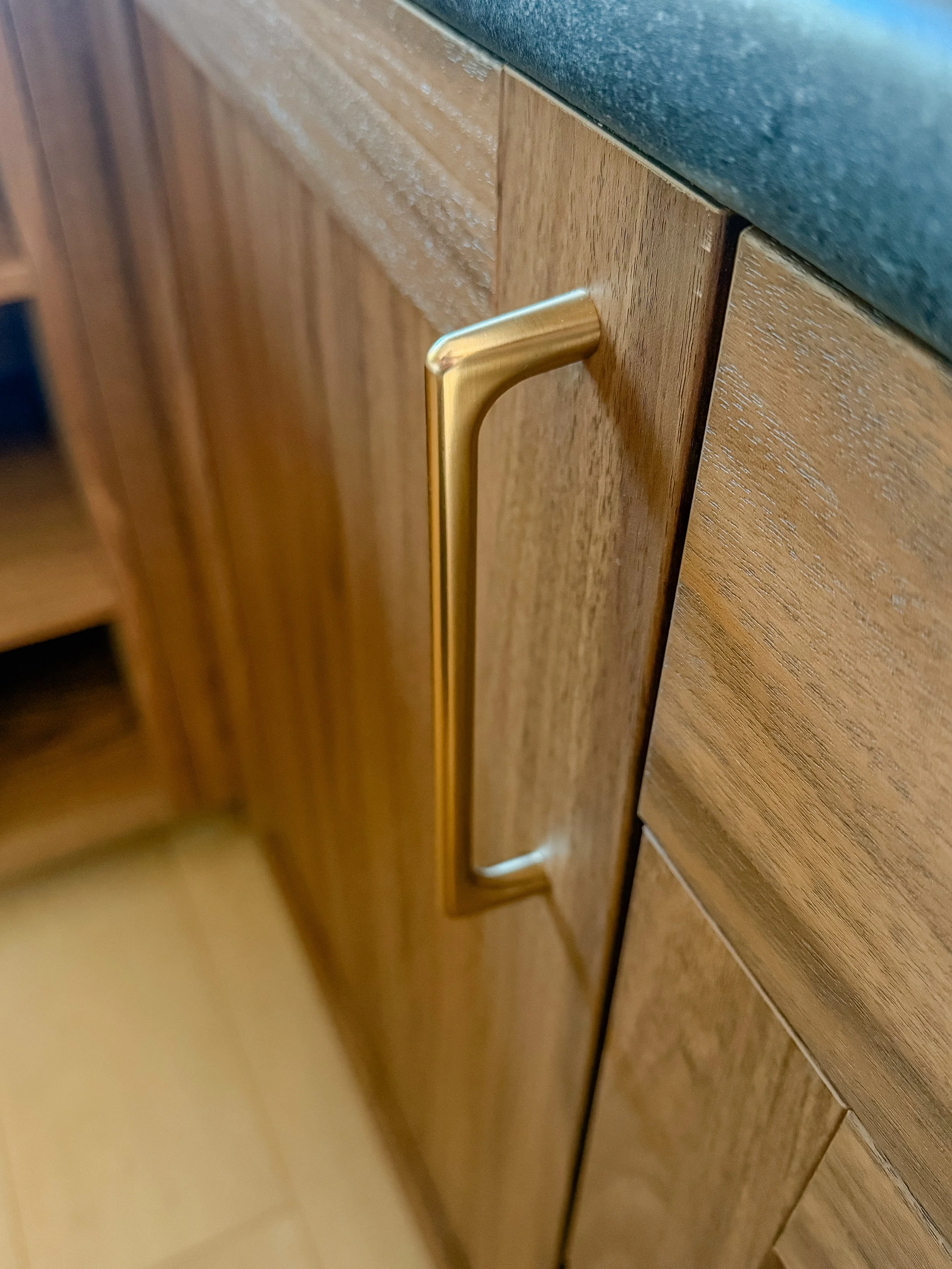 Close-up of a gold-colored cabinet handle on a wooden kitchen cabinet under a green countertop.