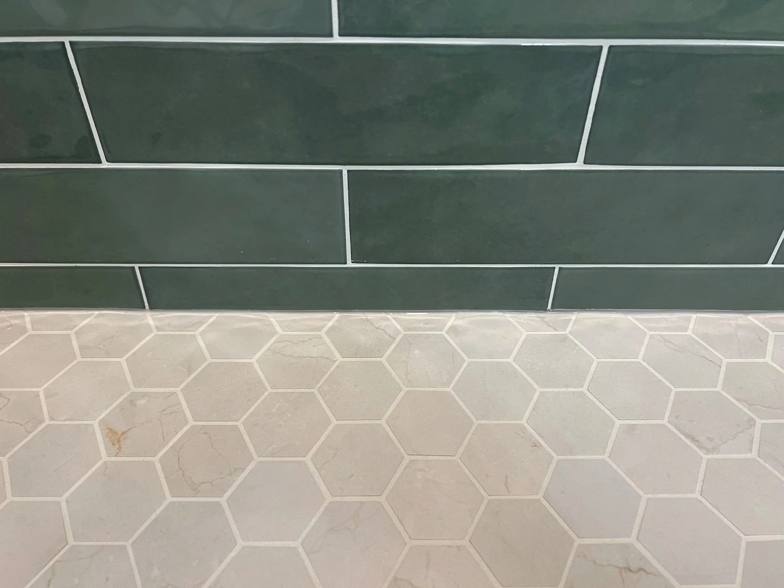 Green rectangular tile wall with white hexagonal tile floor.