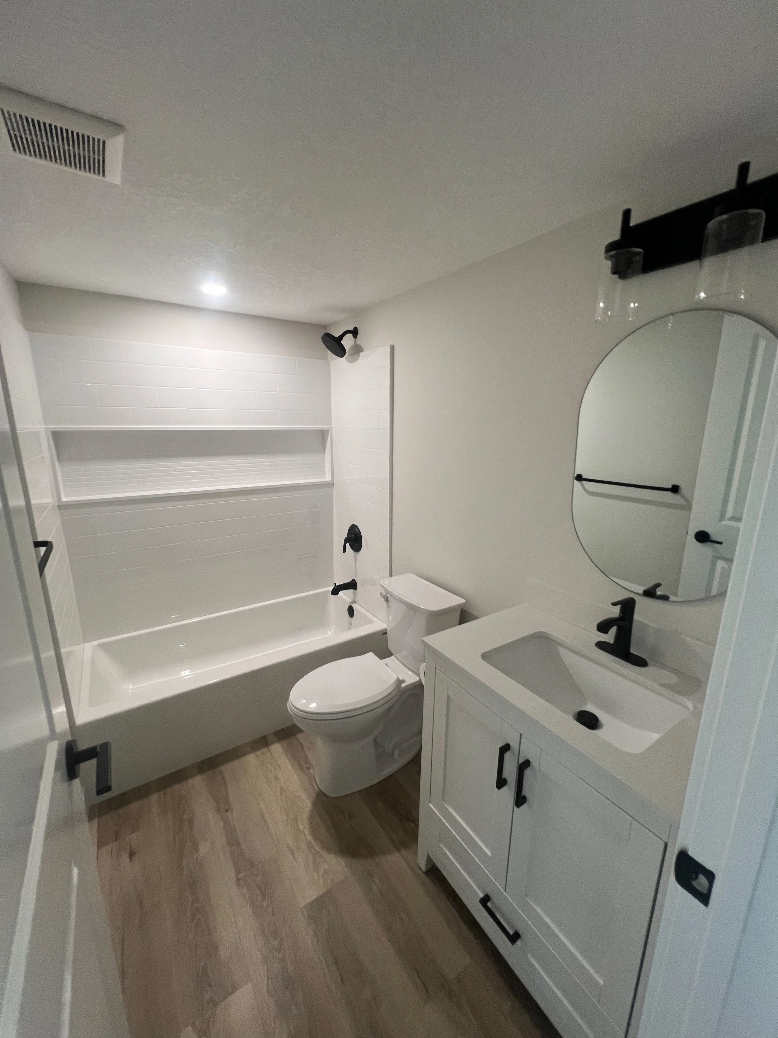 Modern bathroom with bathtub, toilet, and vanity with round mirror.