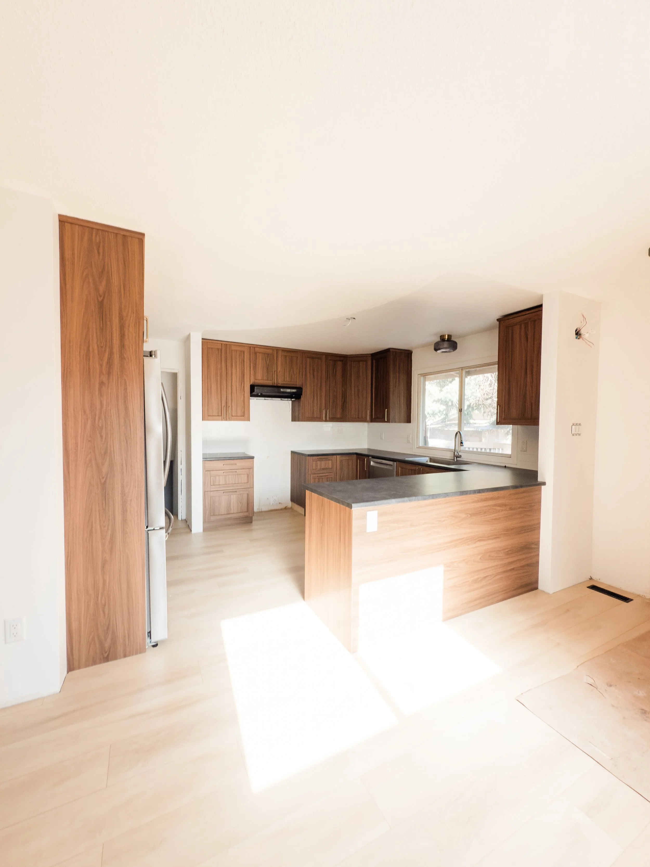Empty kitchen with wooden cabinets, a refrigerator, a window above the sink, and a kitchen island.