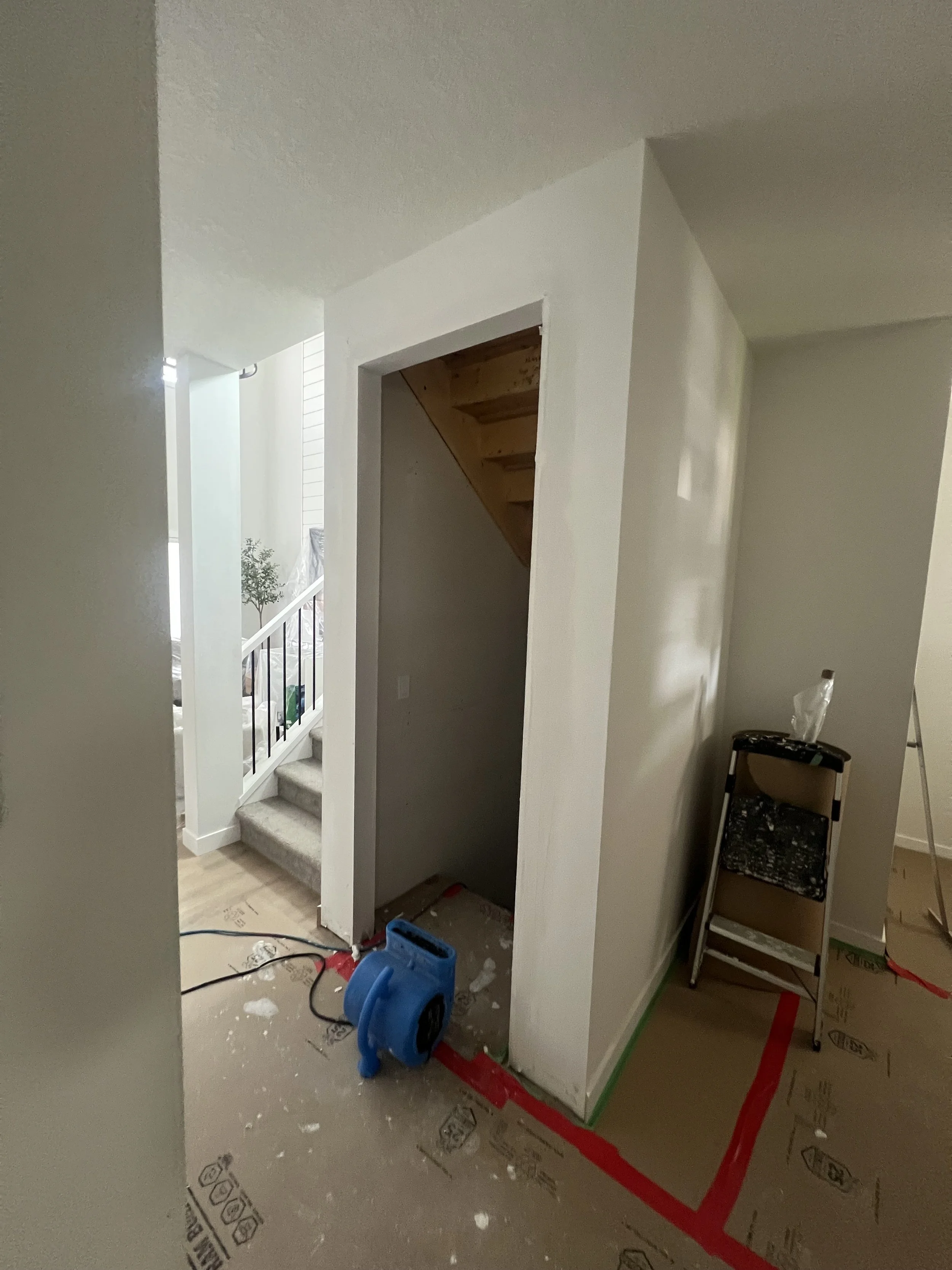 Home renovation with a partially open closet under stairs, covered floors, a blue air mover, and a step ladder.