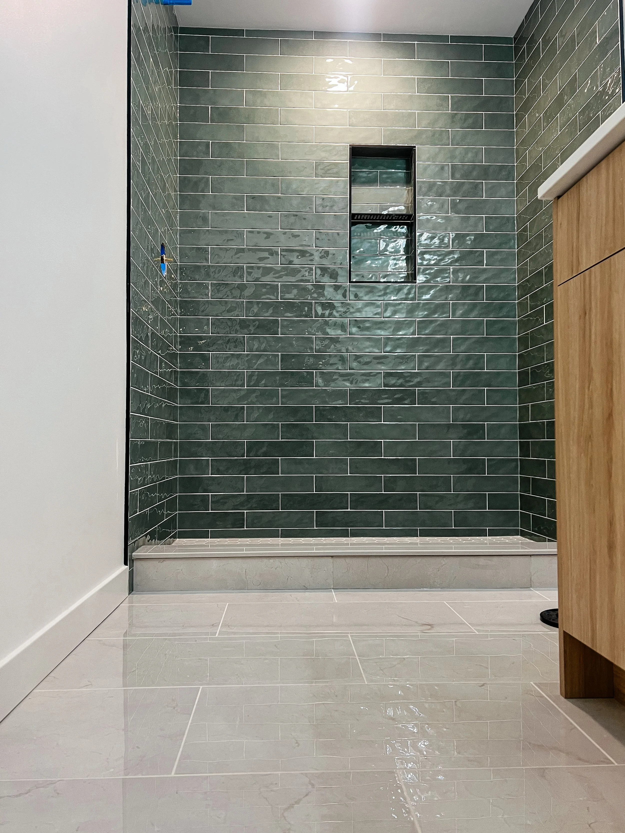 Modern shower with green subway tiles, built-in shelf, and light marble floor tiles.