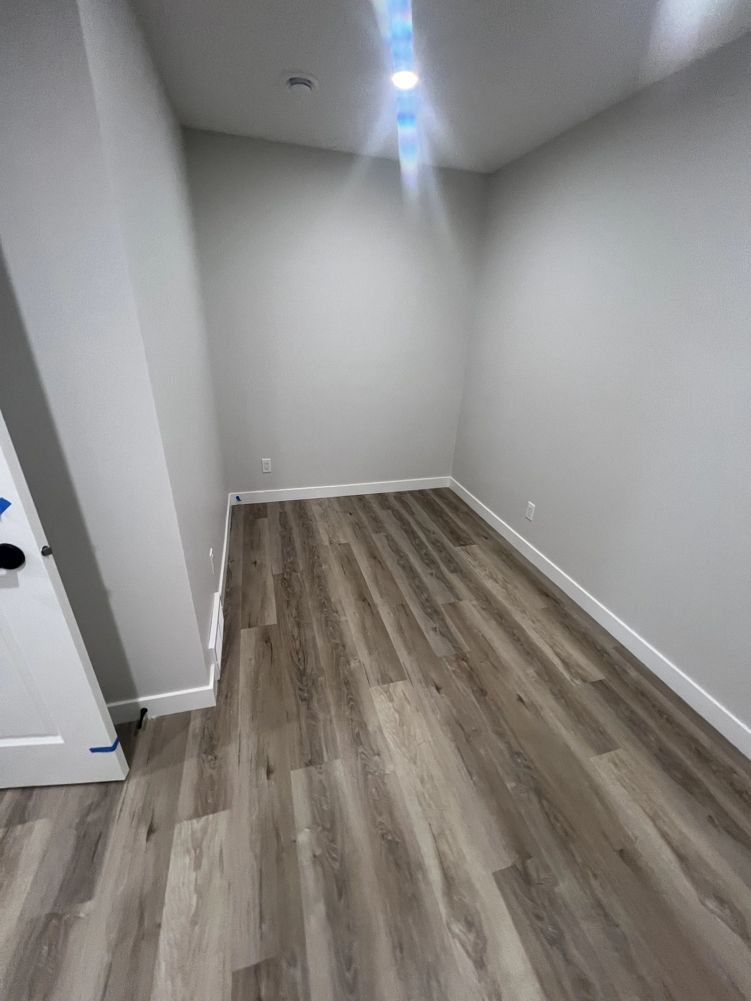 Empty room with light gray walls, wooden floor, and a ceiling light.