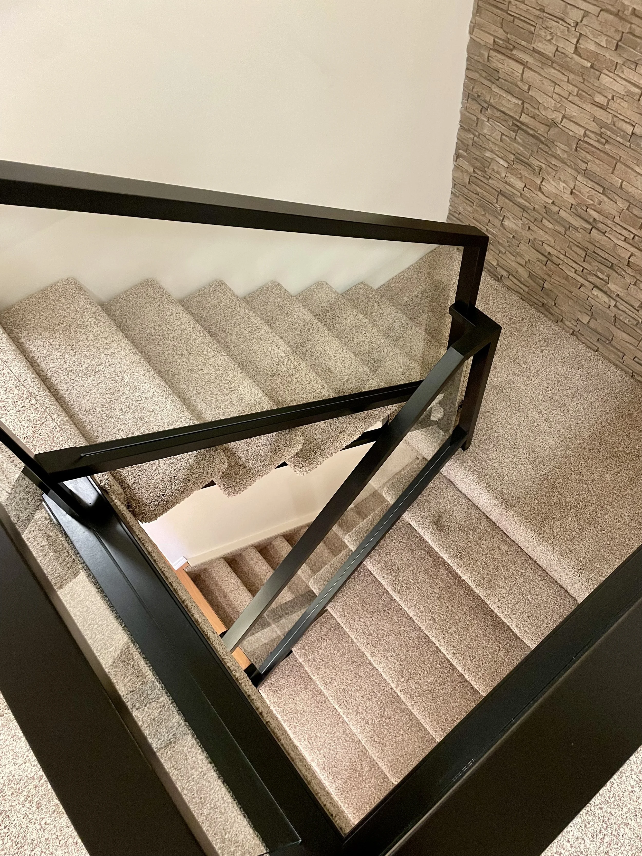 Carpeted staircase with black metal railing and stone accent wall