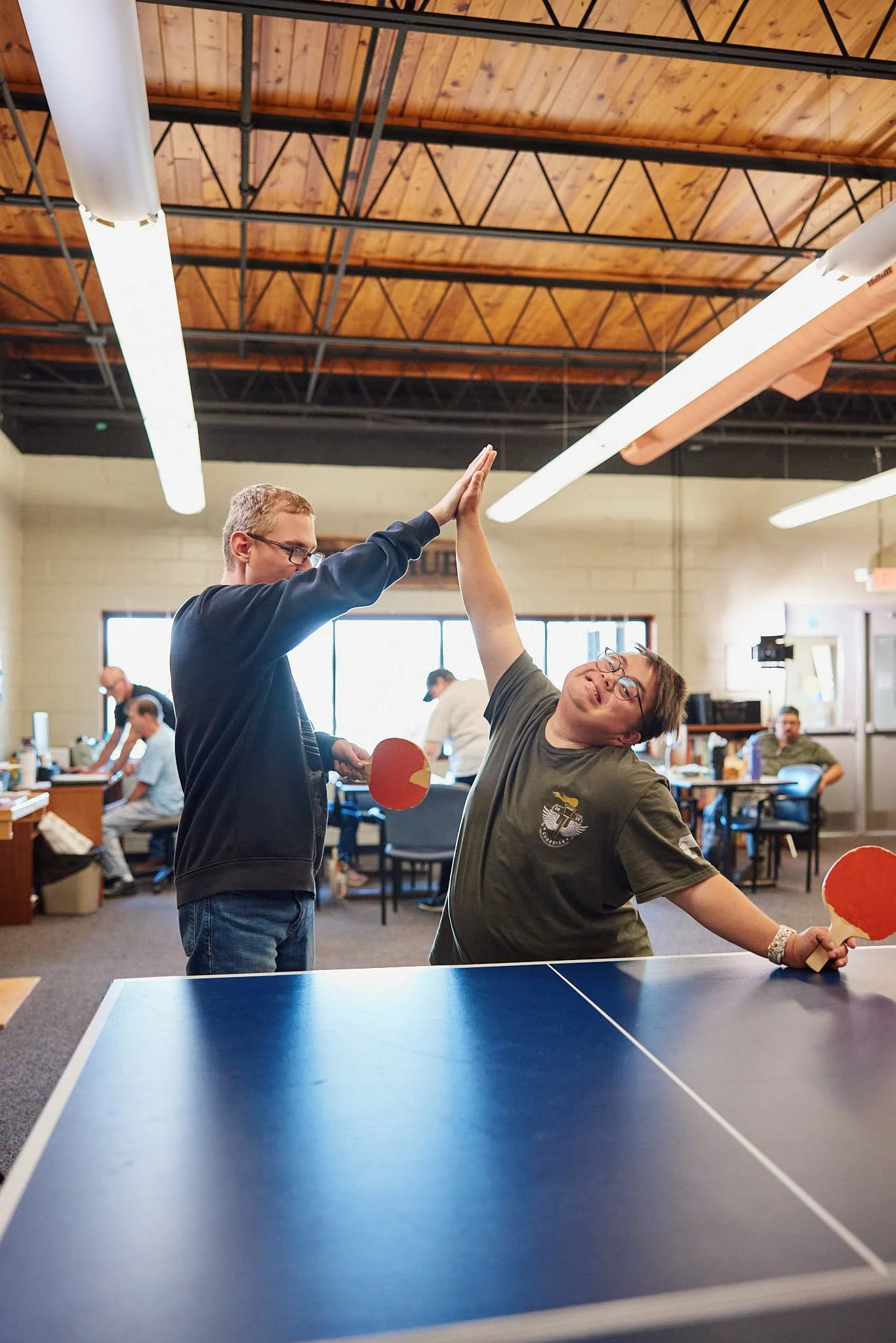 Young man holding a laptop walking outside a facility for day services with greenery and sunlight in the background.