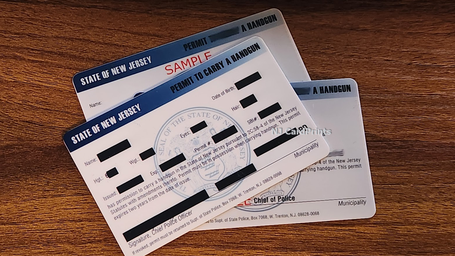 Three New Jersey handgun permits with redacted information, on a wooden surface.