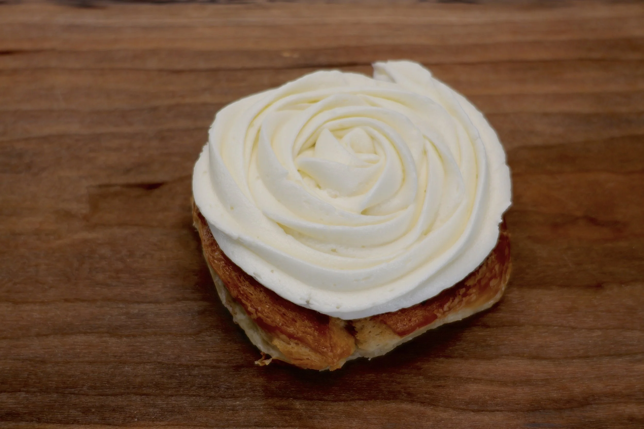 Close-up of a piece of bread topped with swirled white frosting, sitting on a wooden surface.