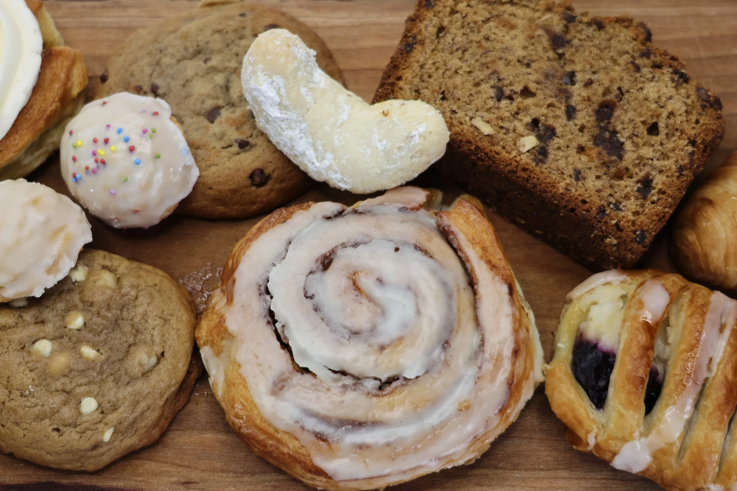 A variety of baked goods, including cookies, cinnamon rolls, and slices of banana bread with chocolate chips.
