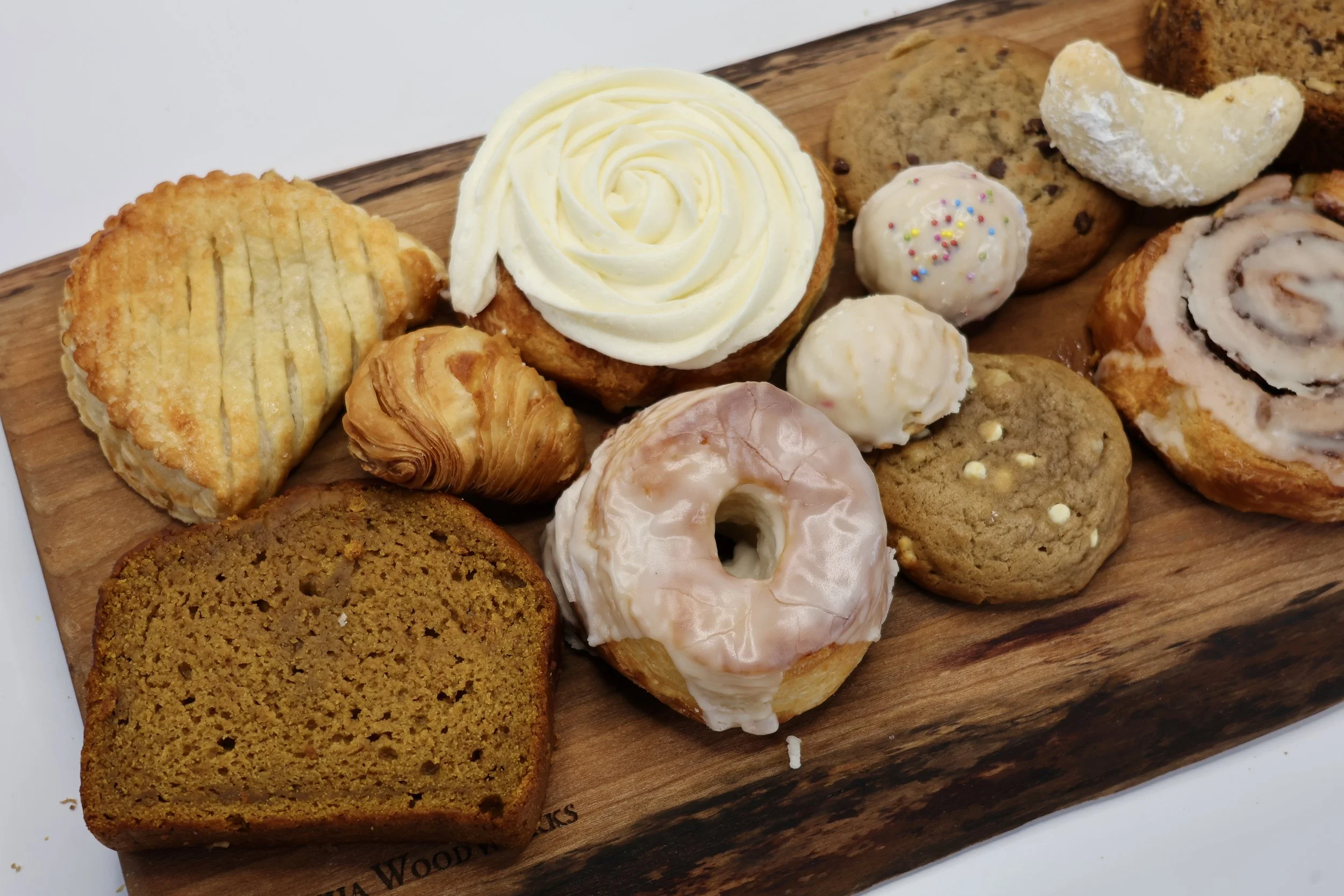Assorted baked goods including cookies, cupcakes, and a muffin on a wooden cutting board.