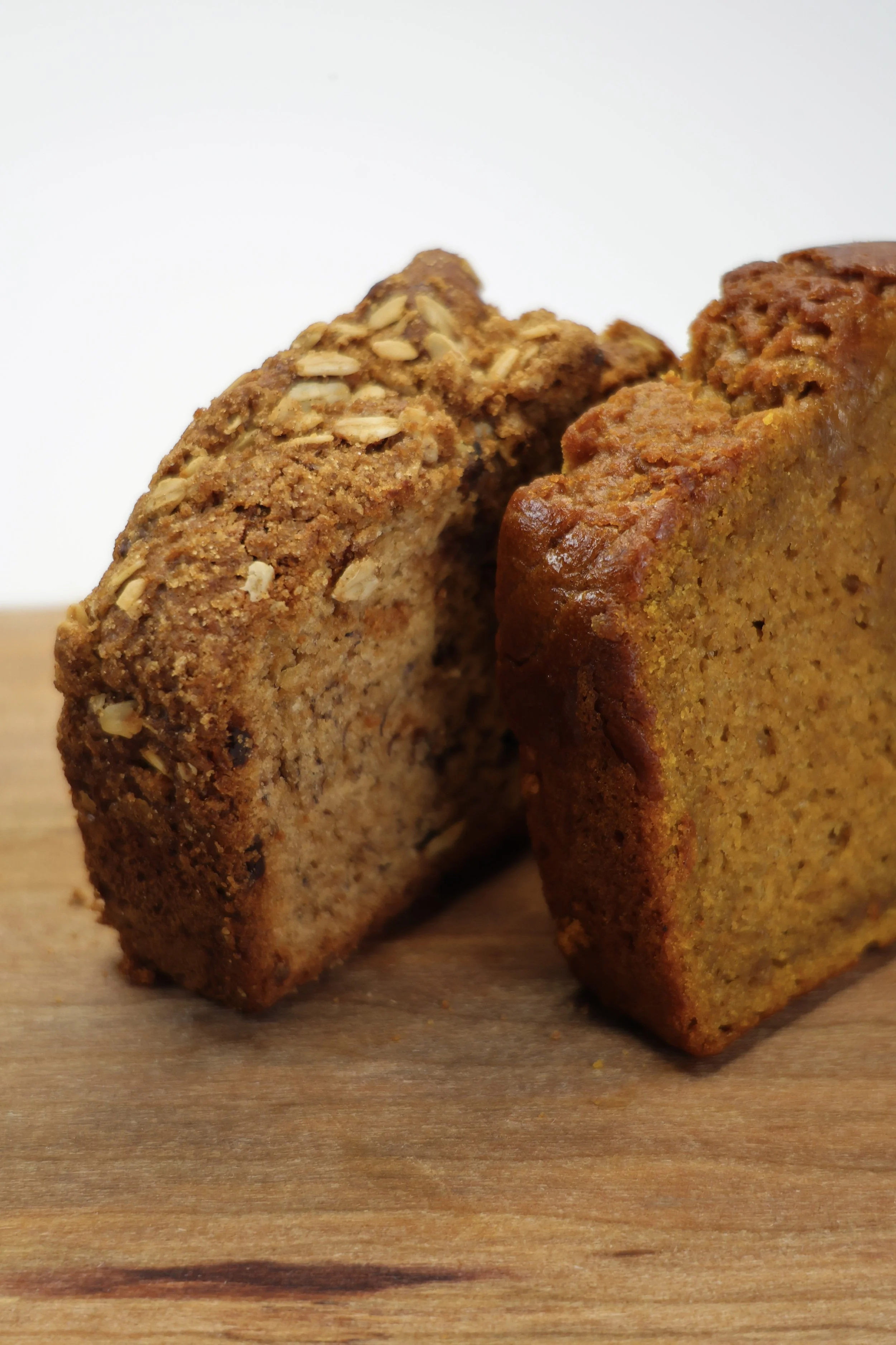 Two slices of banana bread on a wooden surface, one topped with oats.