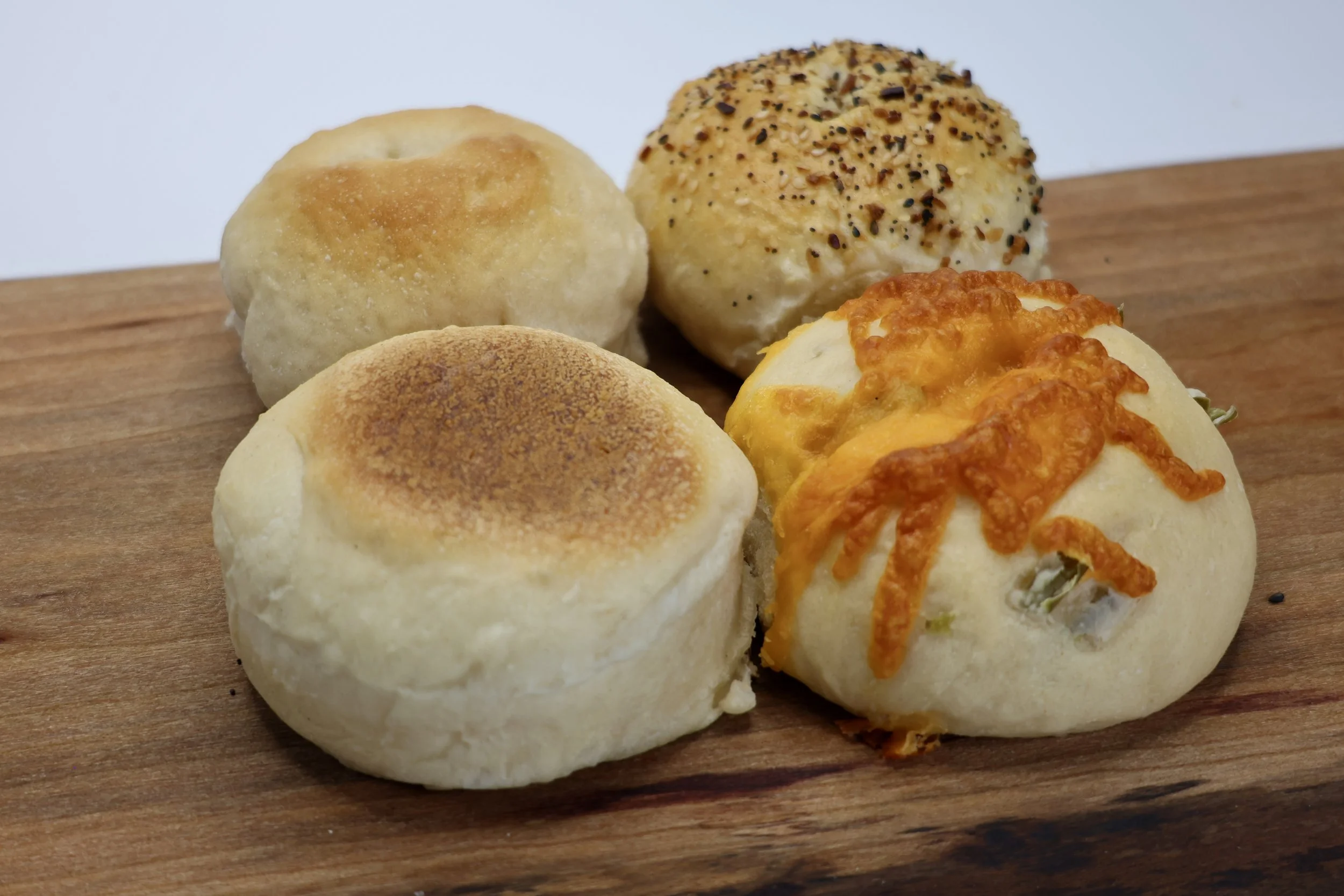 Close-up of four dinner rolls on a wooden surface, with a variety of toppings including sesame seeds, herbs, and cheese.