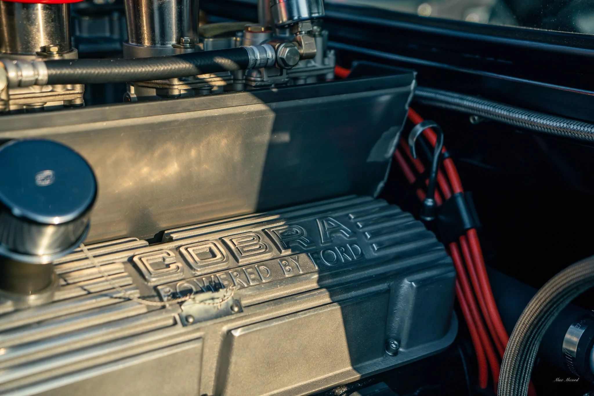 Close-up of a car engine with the brand name 'COBRA' on a silver engine cover and red ignition wires