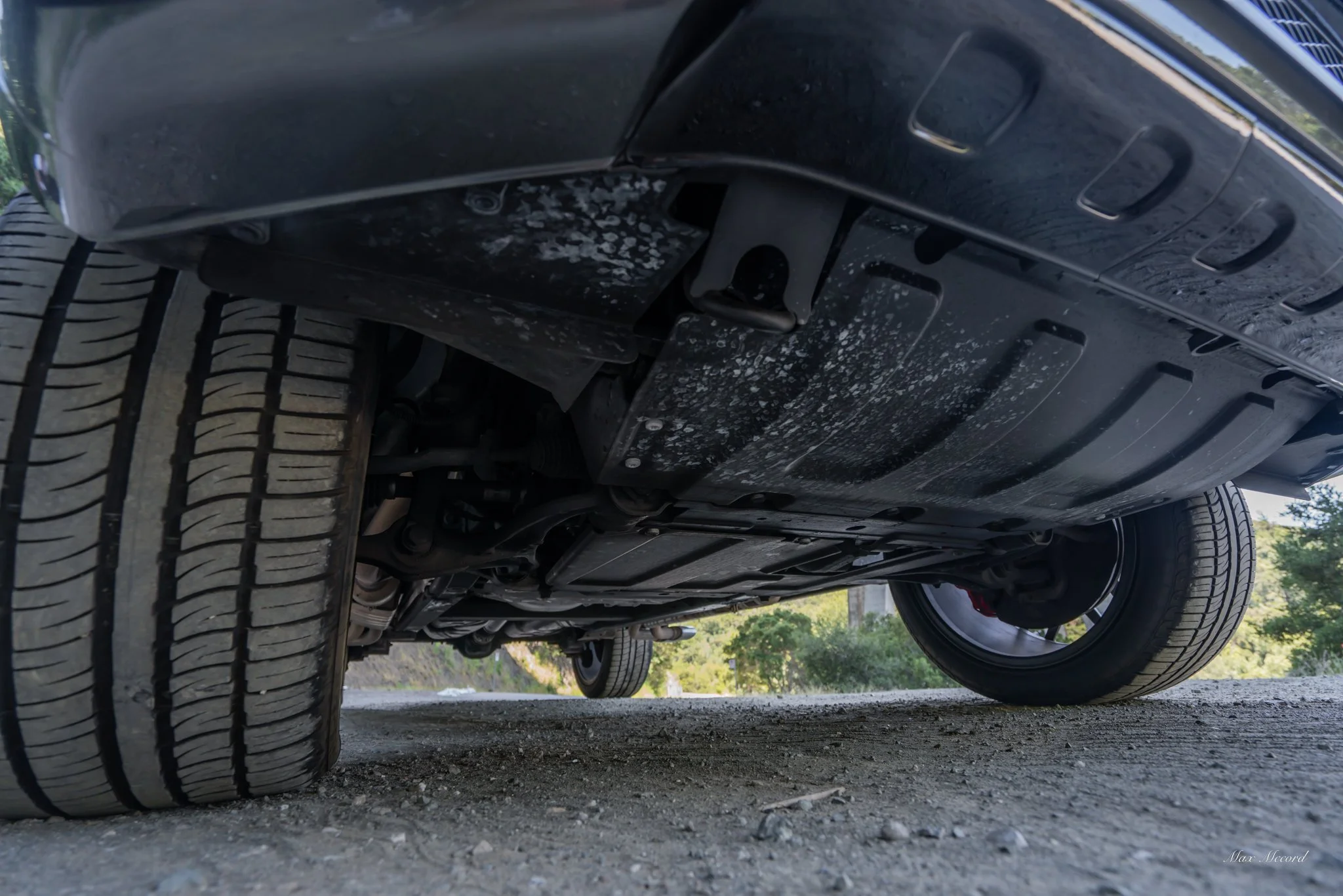 Underneath view of a car showing tires, suspension, and undercarriage with some dirt and splash marks.
