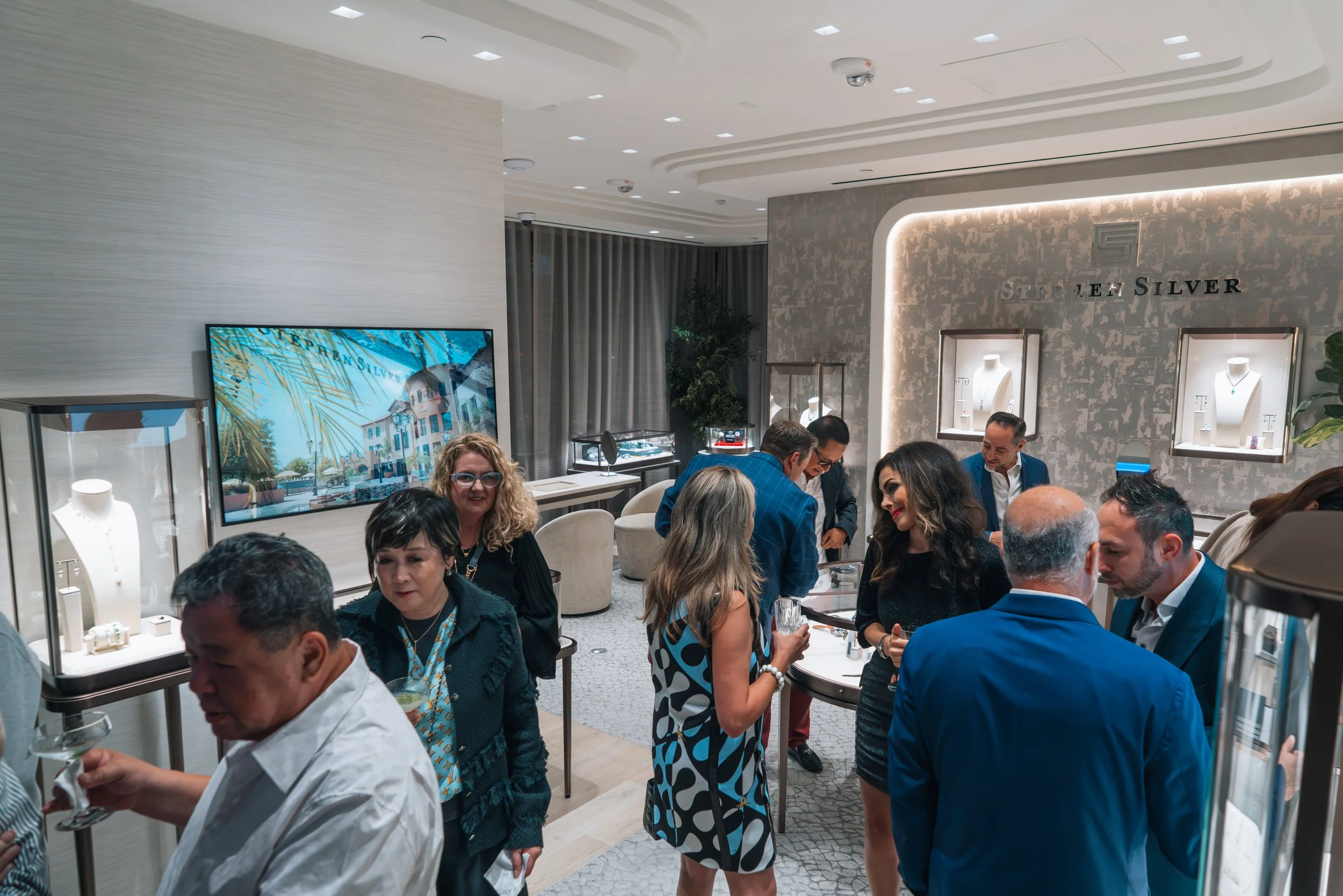 People attending a jewelry event at Stephen Silver jewelry store, showcasing jewelry displays, talking, and socializing in a modern, well-lit retail space.