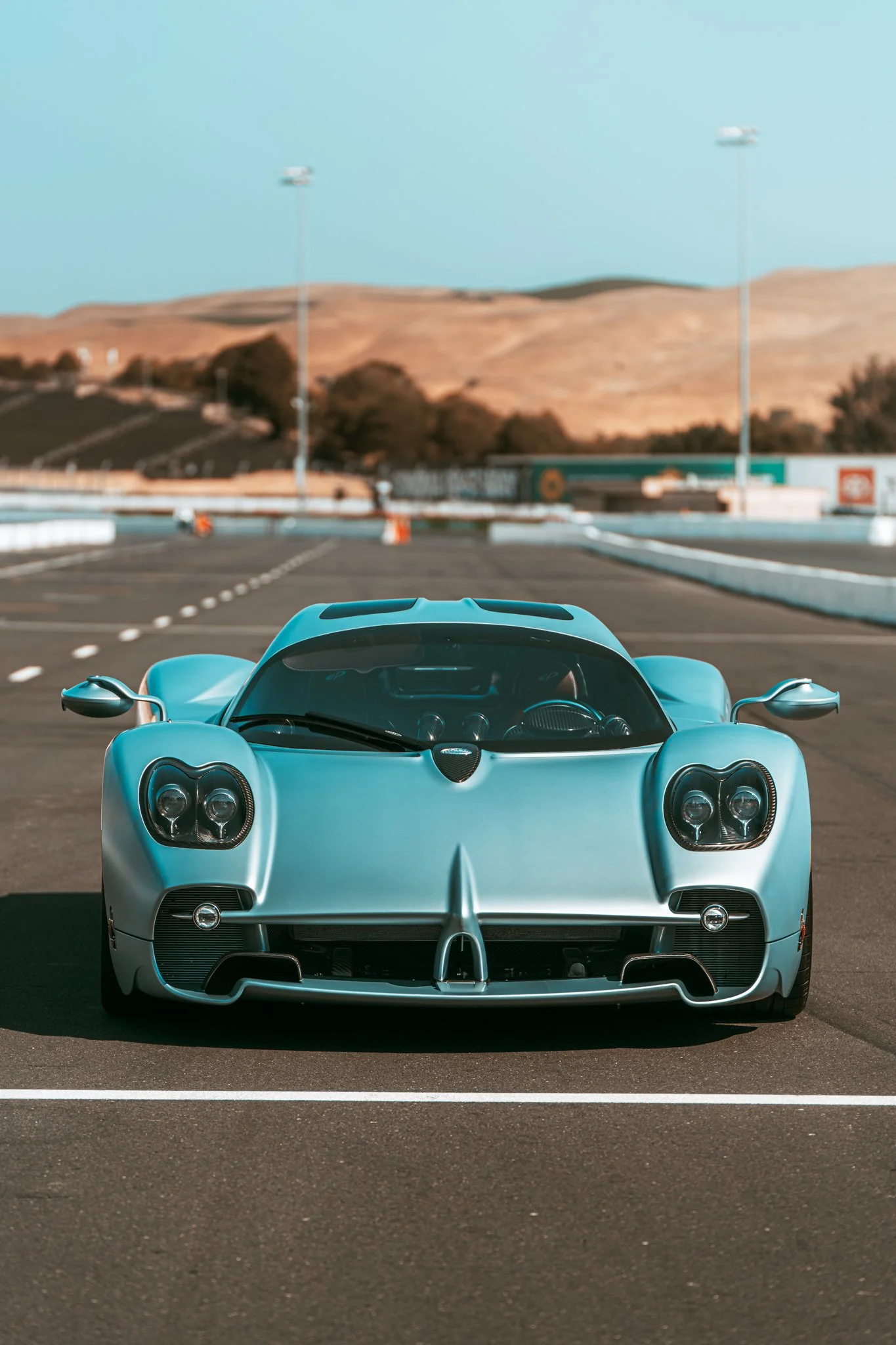 A light blue sports car on a race track with mountains in the background.