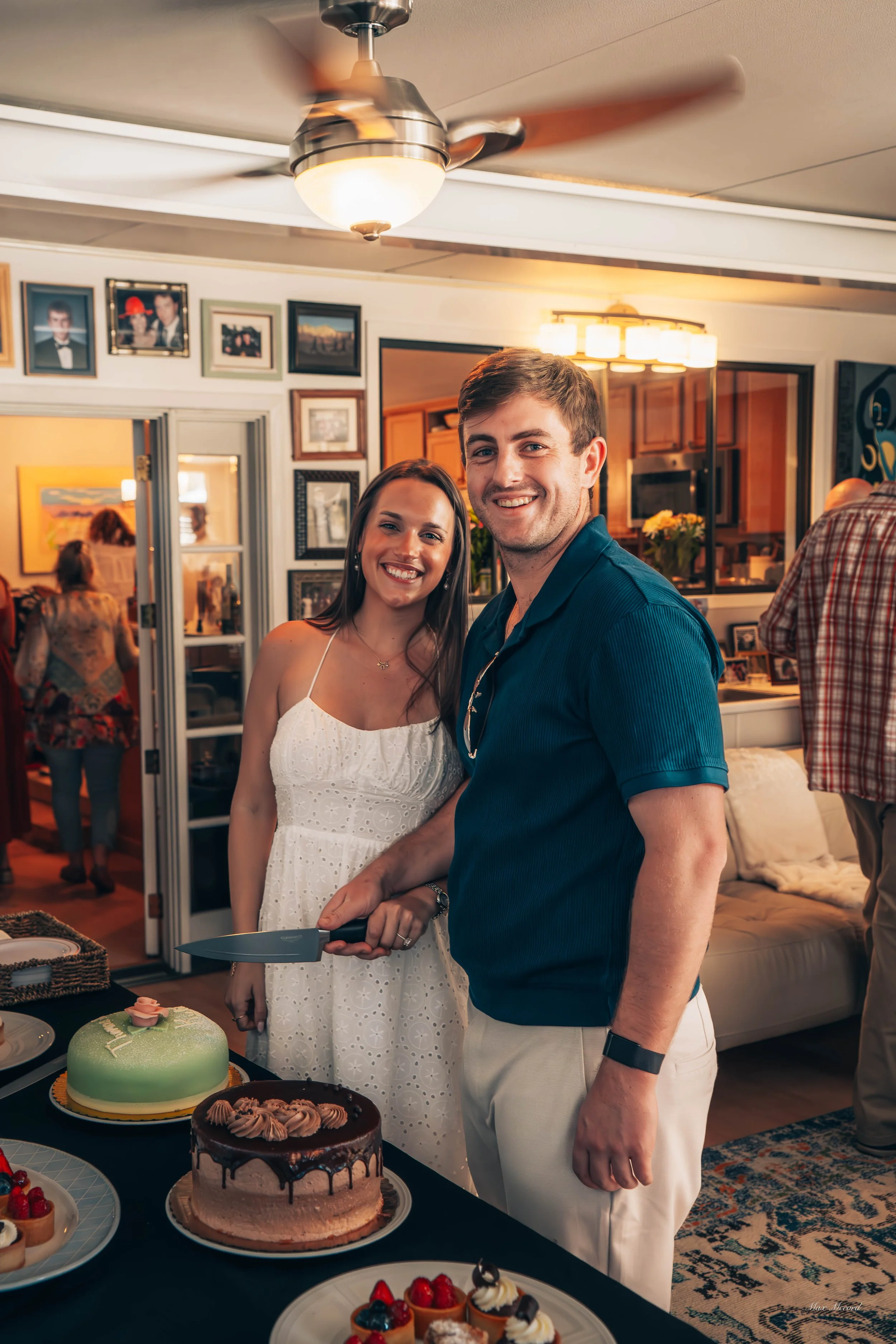 A man and woman smiling at a birthday celebration with cakes and desserts on the table.