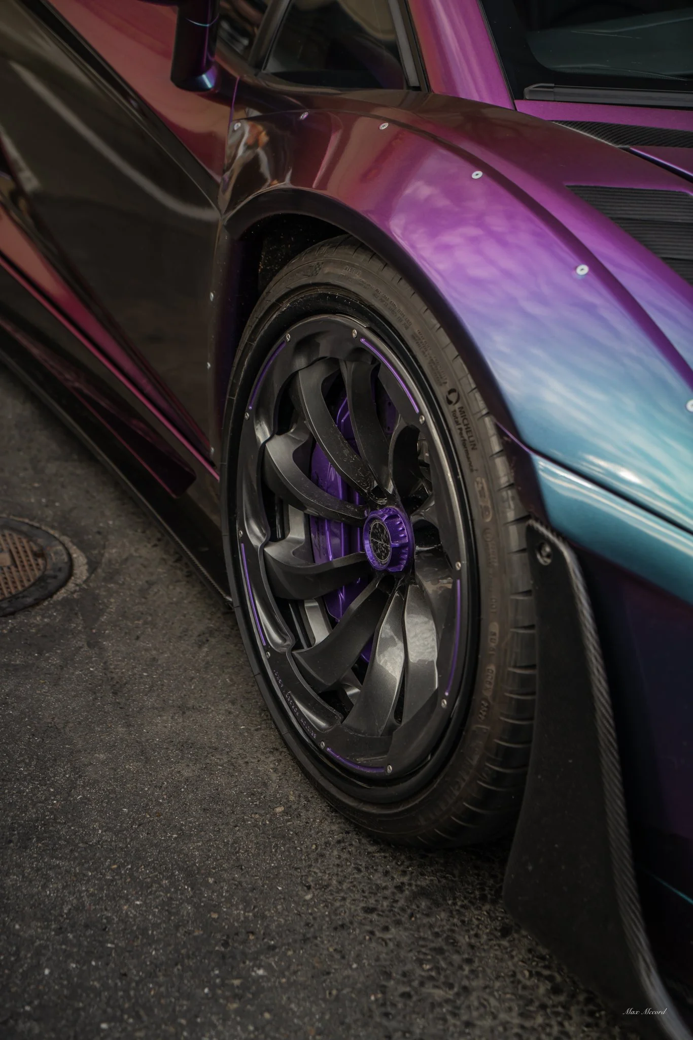 Close-up view of a sleek, colorful sports car with glossy black and purple paint and custom black wheels with purple accents.