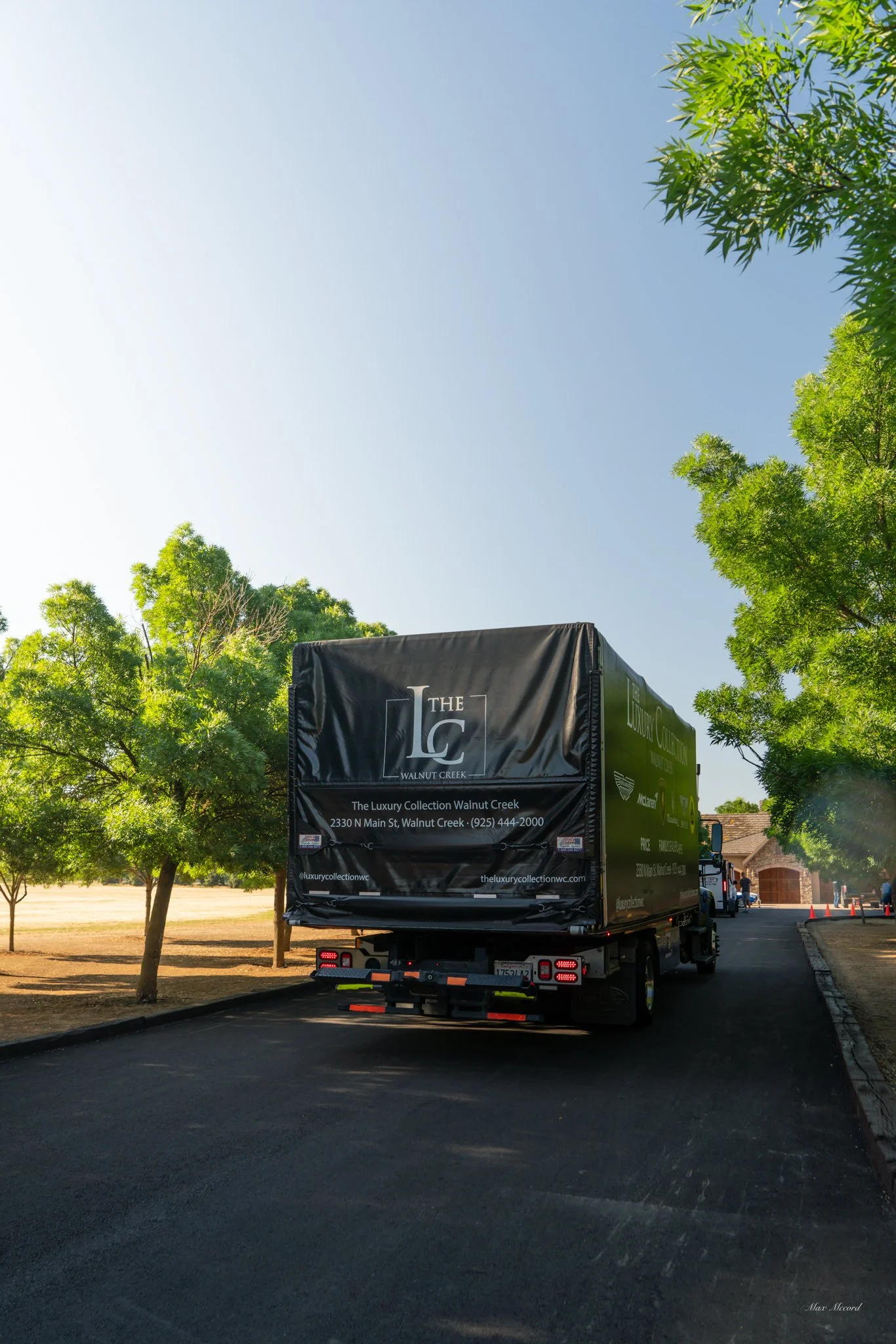 A delivery truck parked on a street with trees on both sides, in clear weather with a blue sky.