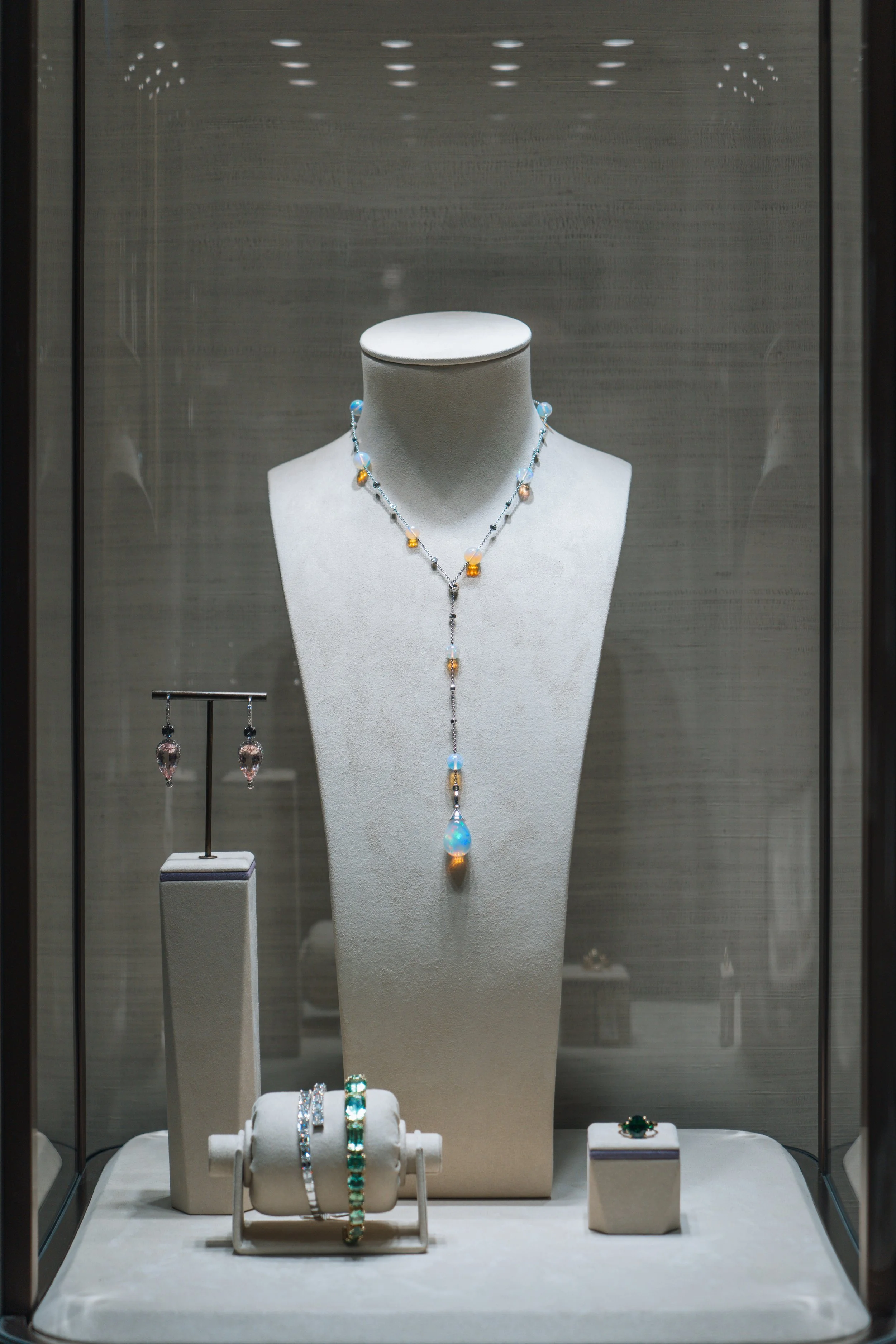 Display case with jewelry including a necklace, earrings, and rings, arranged on a mannequin bust and jewelry stands.