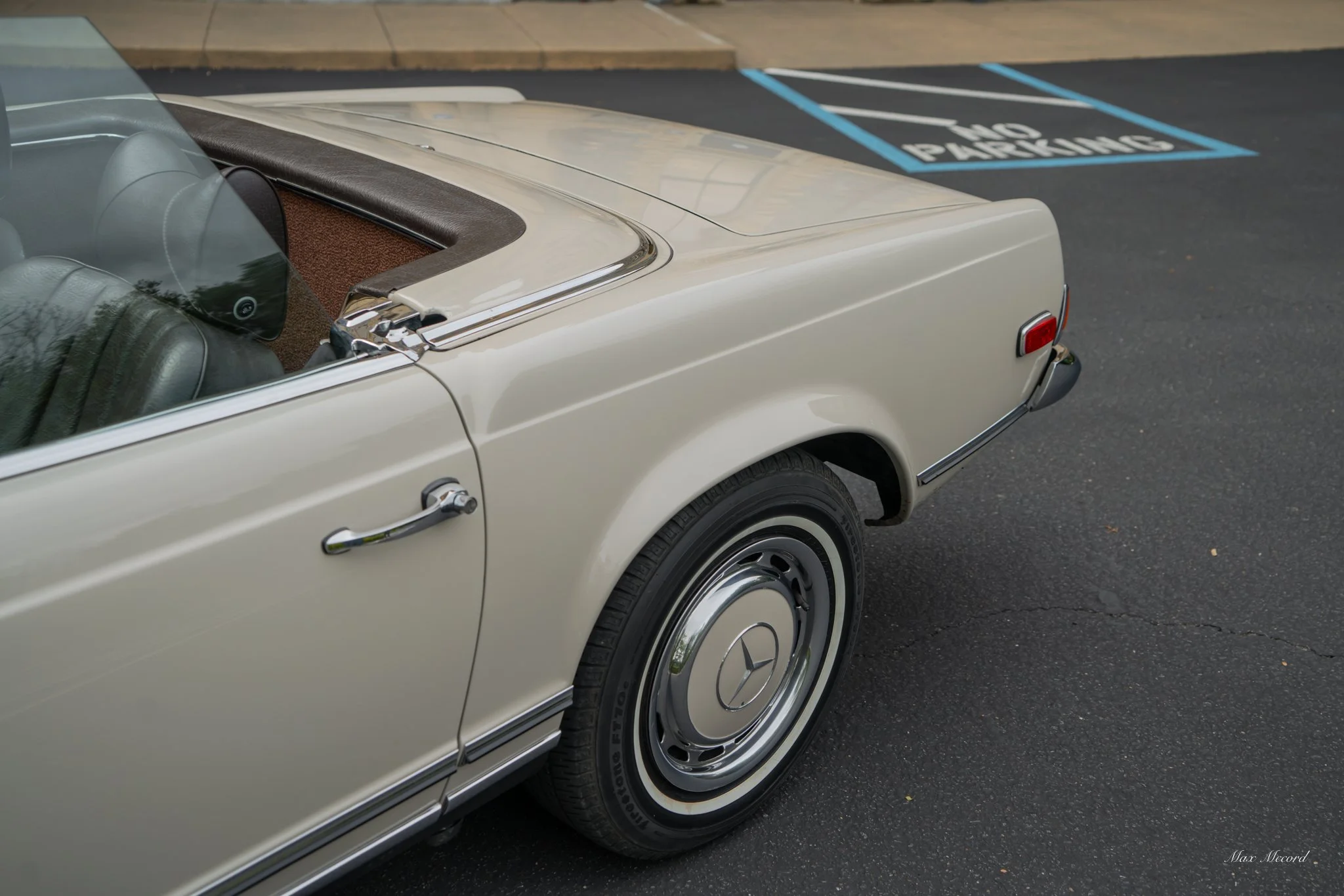 Close-up of a vintage cream-colored Mercedes-Benz car parked in a parking lot near a 'No Parking' space.