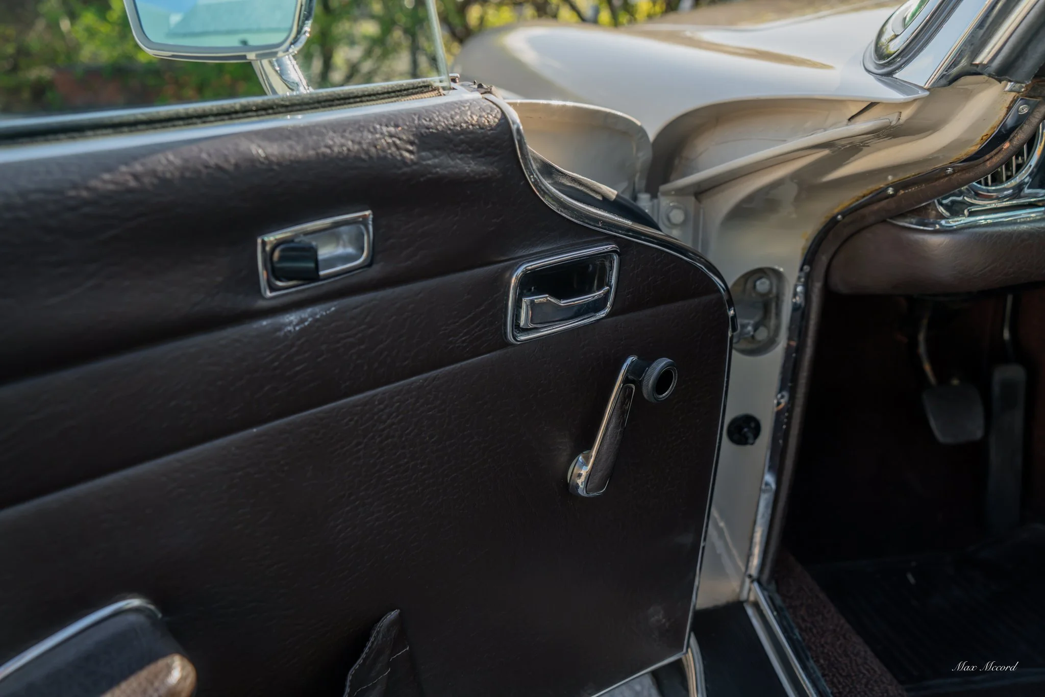 Close-up of the interior of a vintage car, showing the black dashboard, window crank, and part of the door.