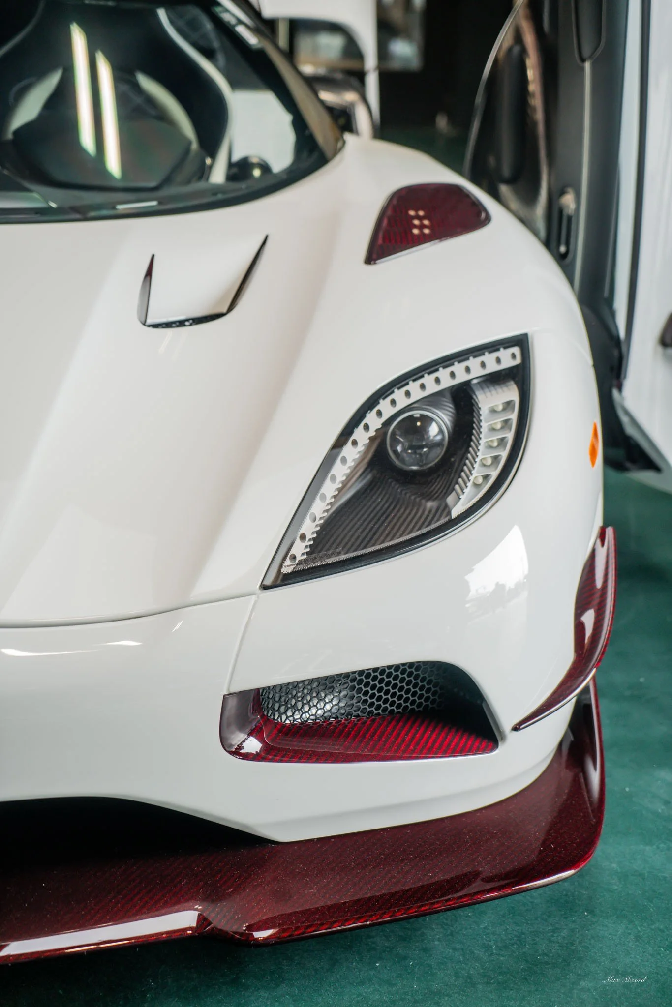Close-up of the front of a white sports car with intricate headlight design, red accents, and a carbon-fiber front splitter.