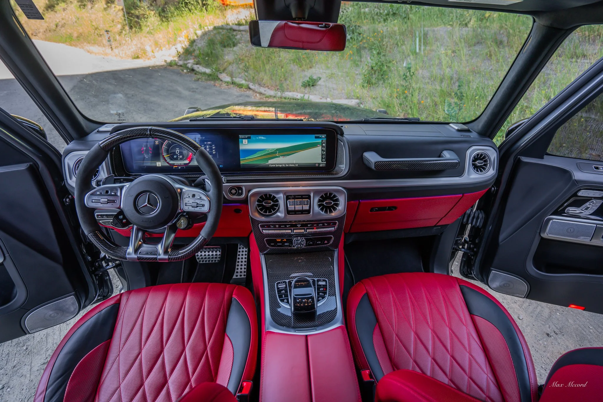 Interior of a luxury Mercedes-Benz vehicle with a digital dashboard, a wide touchscreen display, and red leather seats with quilted stitching.