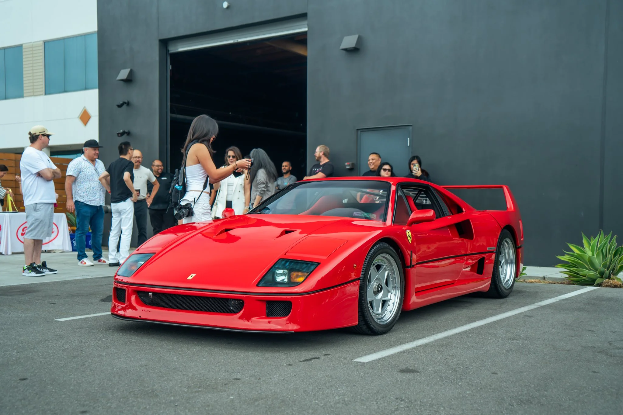 Red Ferrari F40 sports car parked in front of a group of people outside a building.