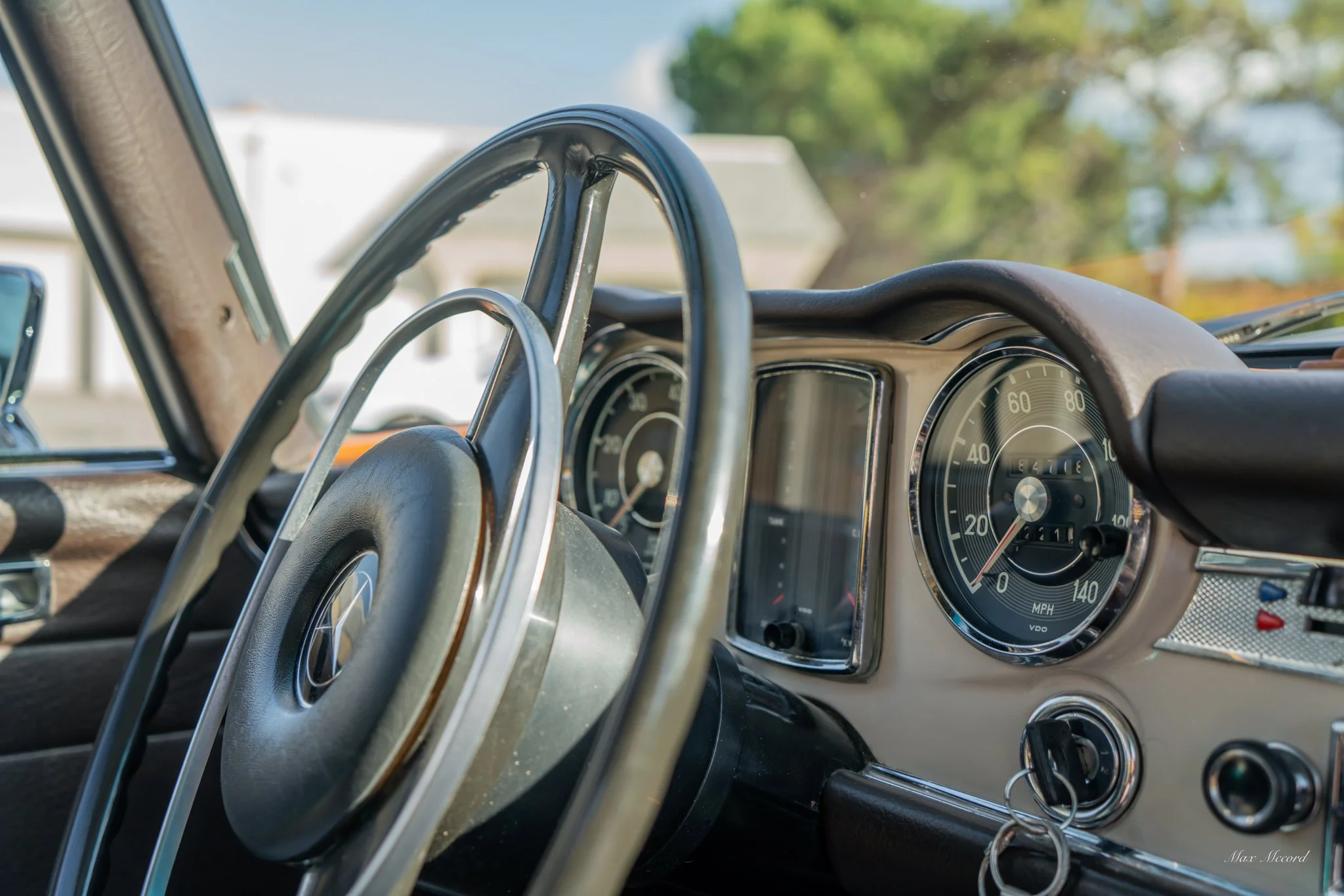 Close-up of the dashboard and steering wheel of a vintage Mercedes-Benz car, with an analog speedometer, odometer, and other gauges.