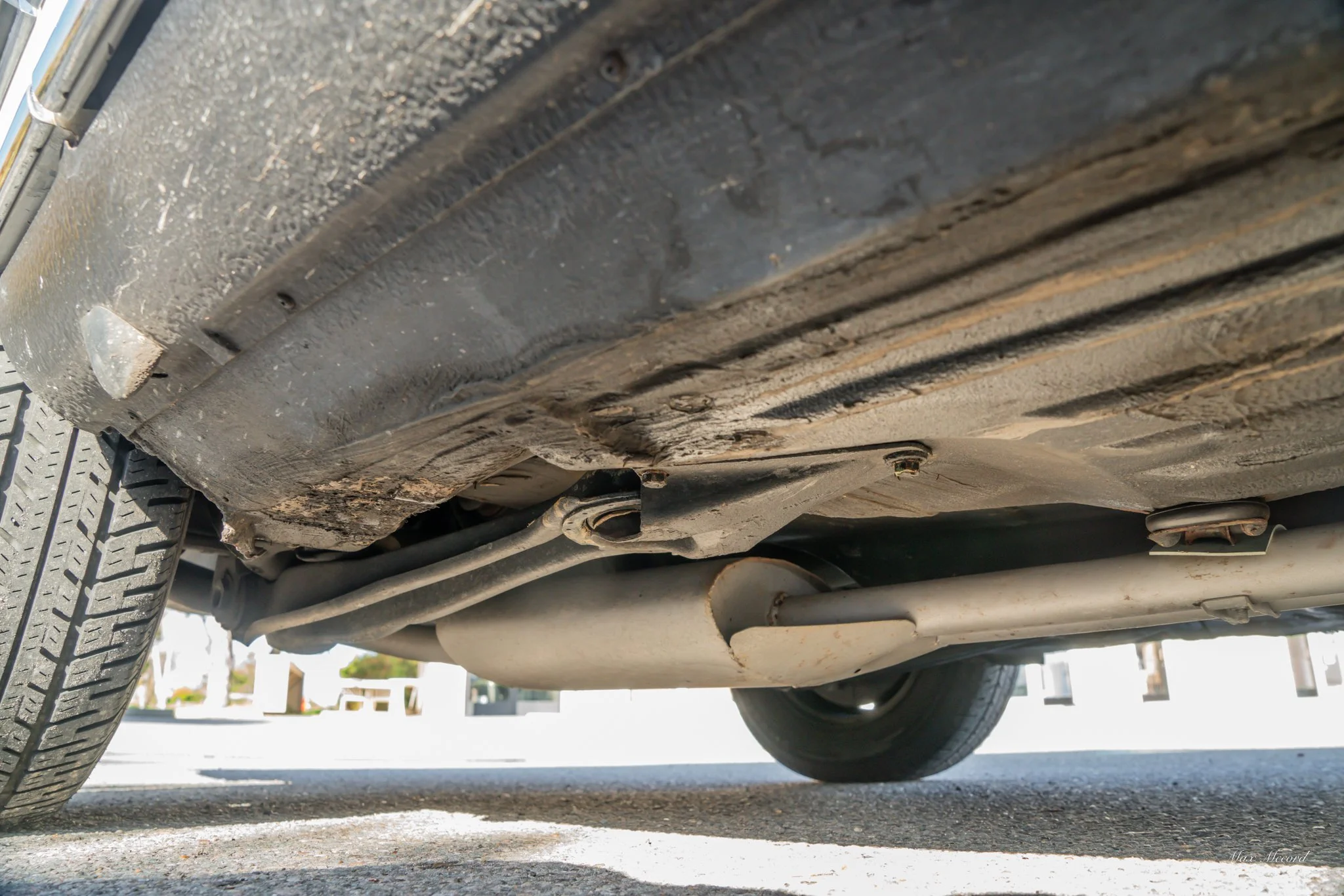 Underneath view of a car showing the oil pan, exhaust pipe, and part of the tire.