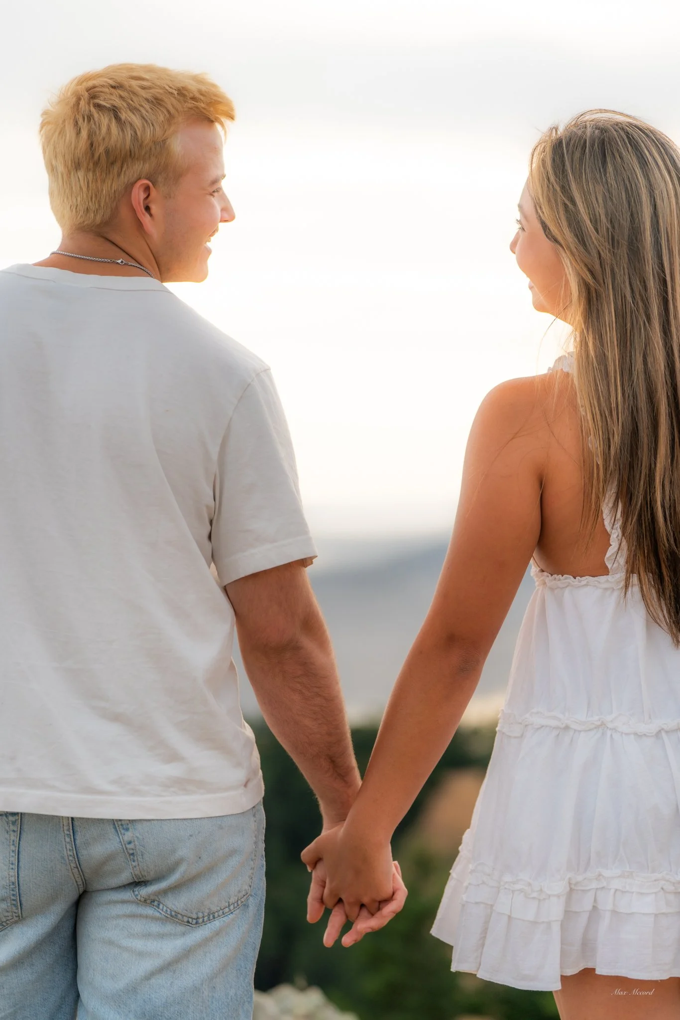 A young couple holding hands and smiling at each other outdoors during daylight.