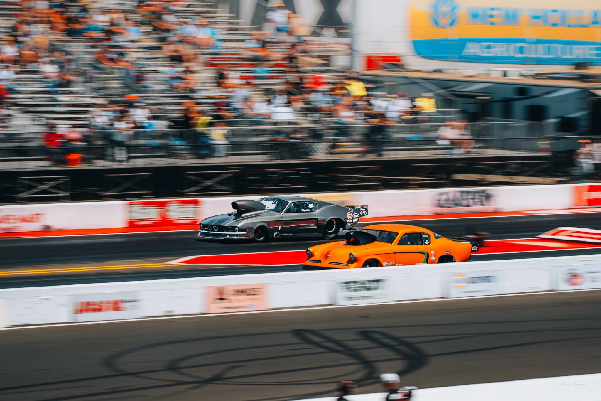 Two drag racing cars on the track with blurred spectators in the background.