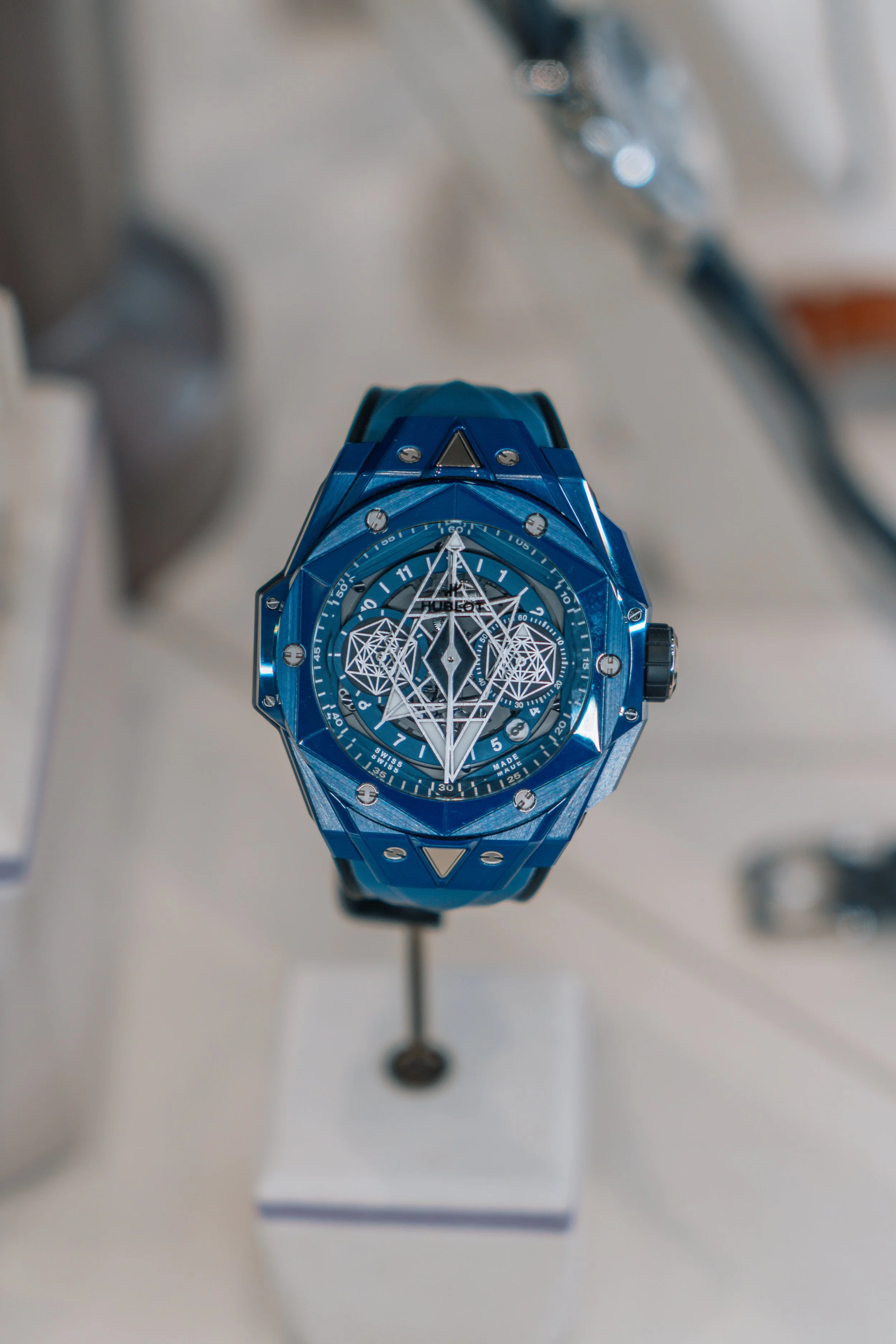 A blue luxury wristwatch with an intricate geometric and spider-web design on the dial.