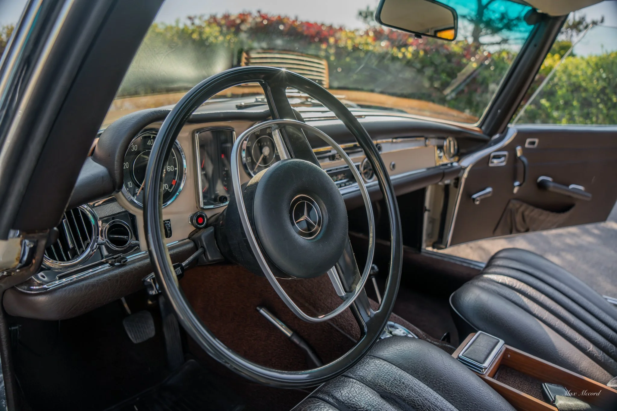 Interior of a vintage Mercedes-Benz car, showing the steering wheel with the Mercedes logo, analog gauges, and dashboard details.