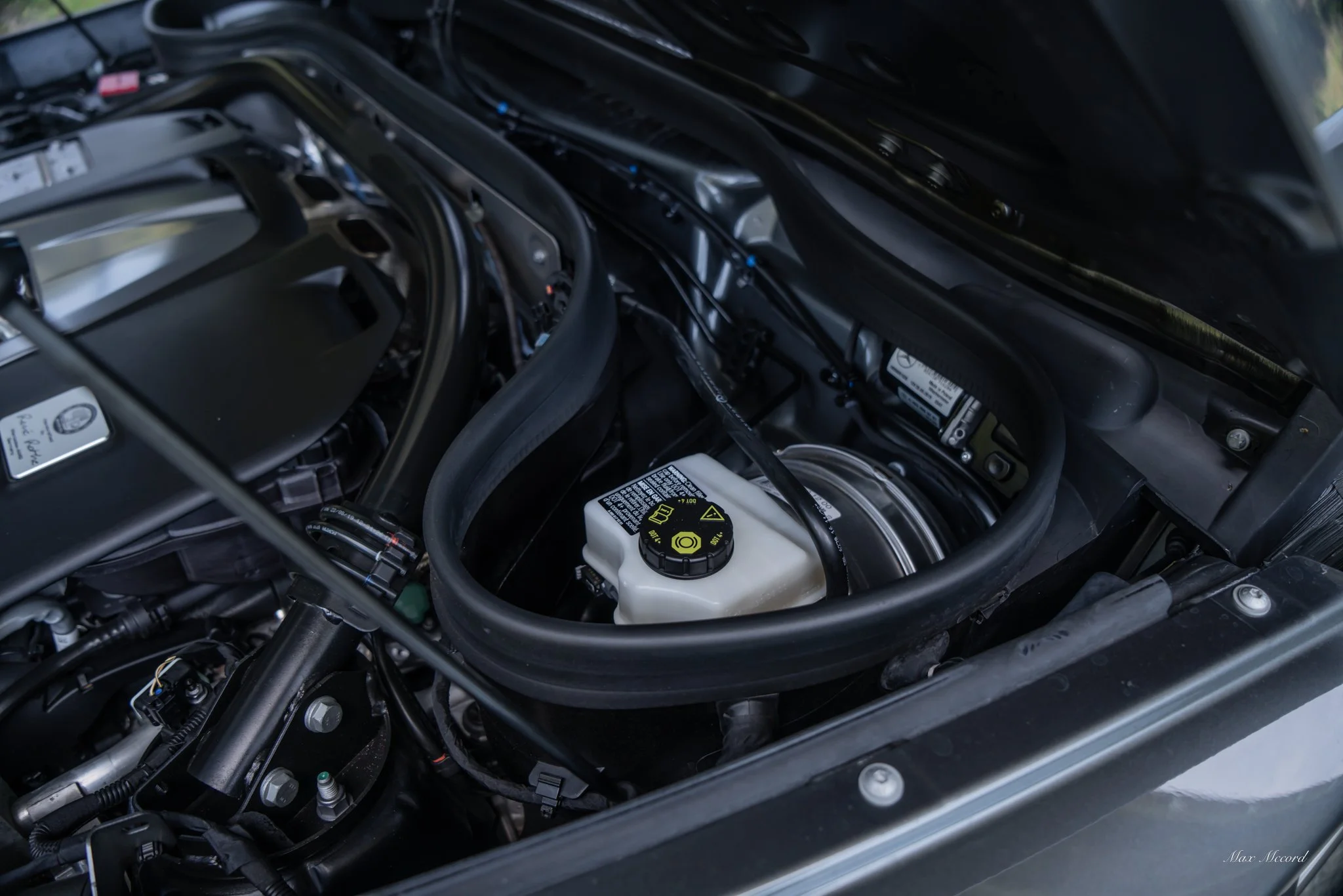 Close-up of car engine with various components and a white coolant reservoir.
