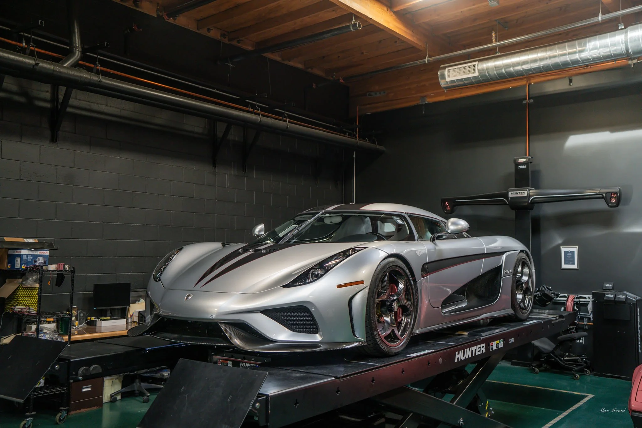 A silver sports car with black and red stripes parked on a hydraulic lift inside a garage.