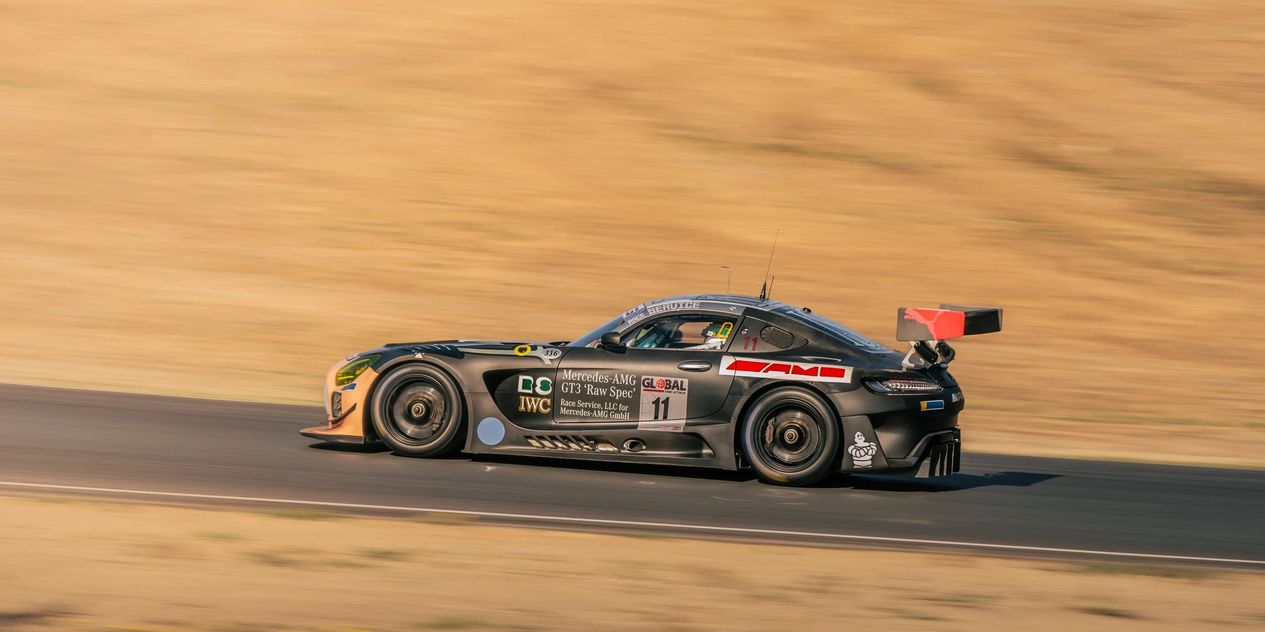 A black race car with sponsorship stickers, numbered 11, driving at high speed on a racetrack with a blurred background.