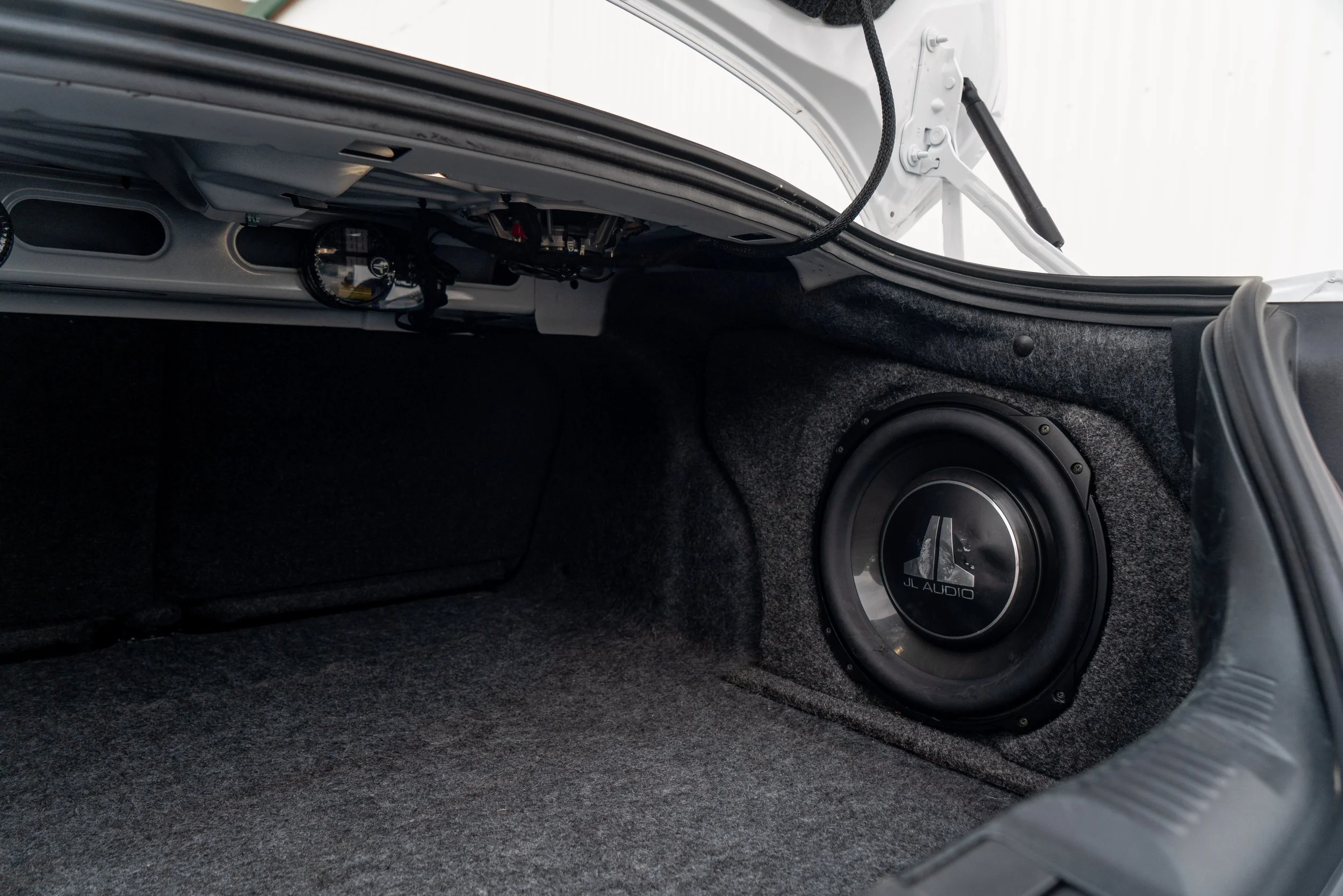 Interior of a car trunk with a JL Audio subwoofer installed in the side panel.