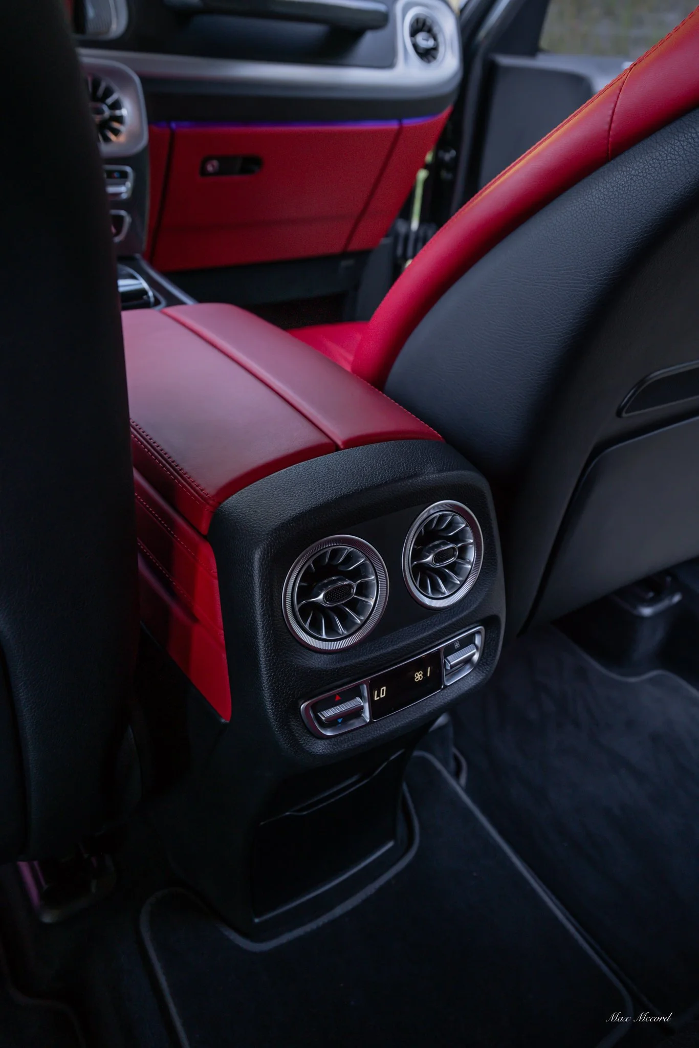 The backseat of a luxury car with black and red leather seats and adjustable climate control vents.